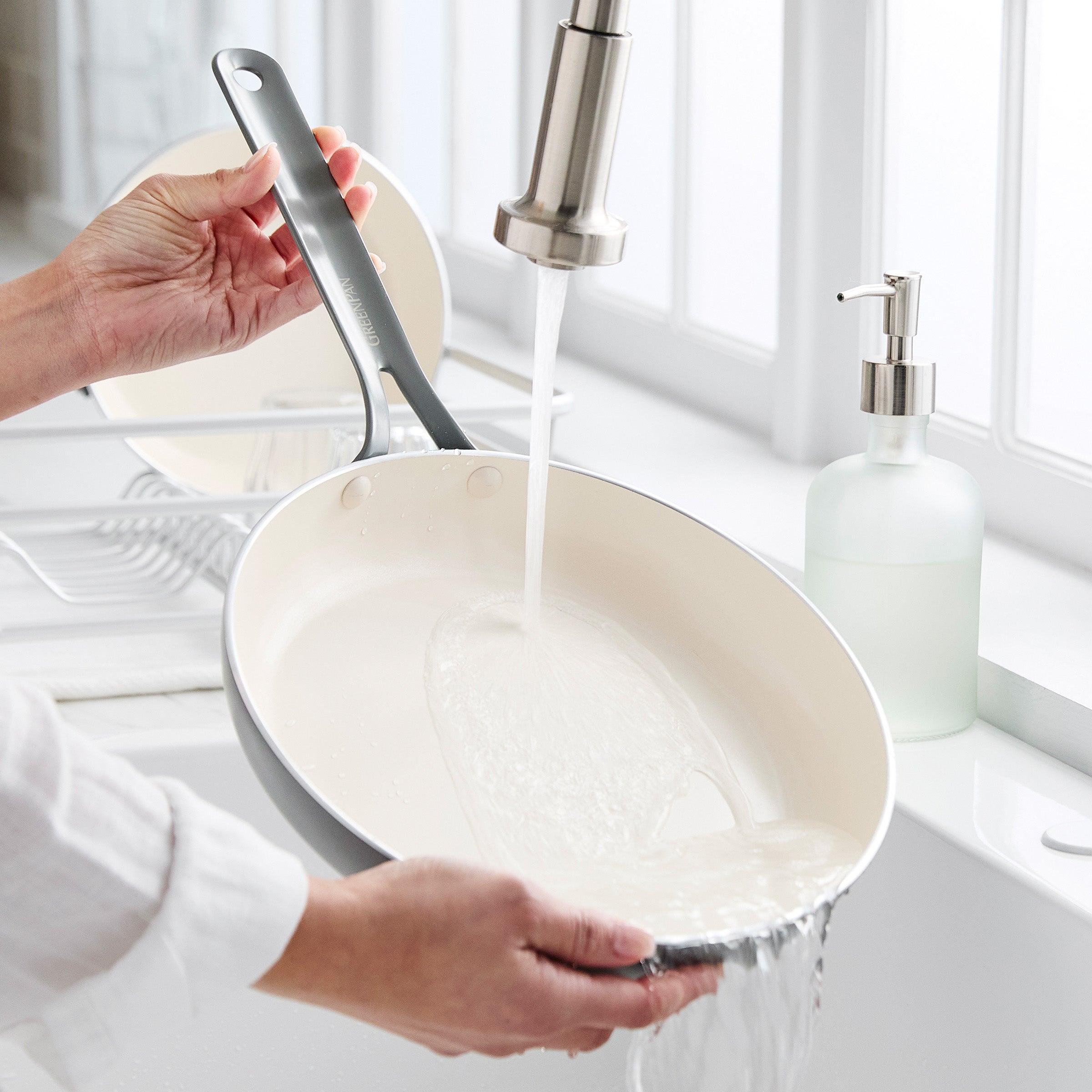 Person washing a frying pan under running water from a kitchen sink