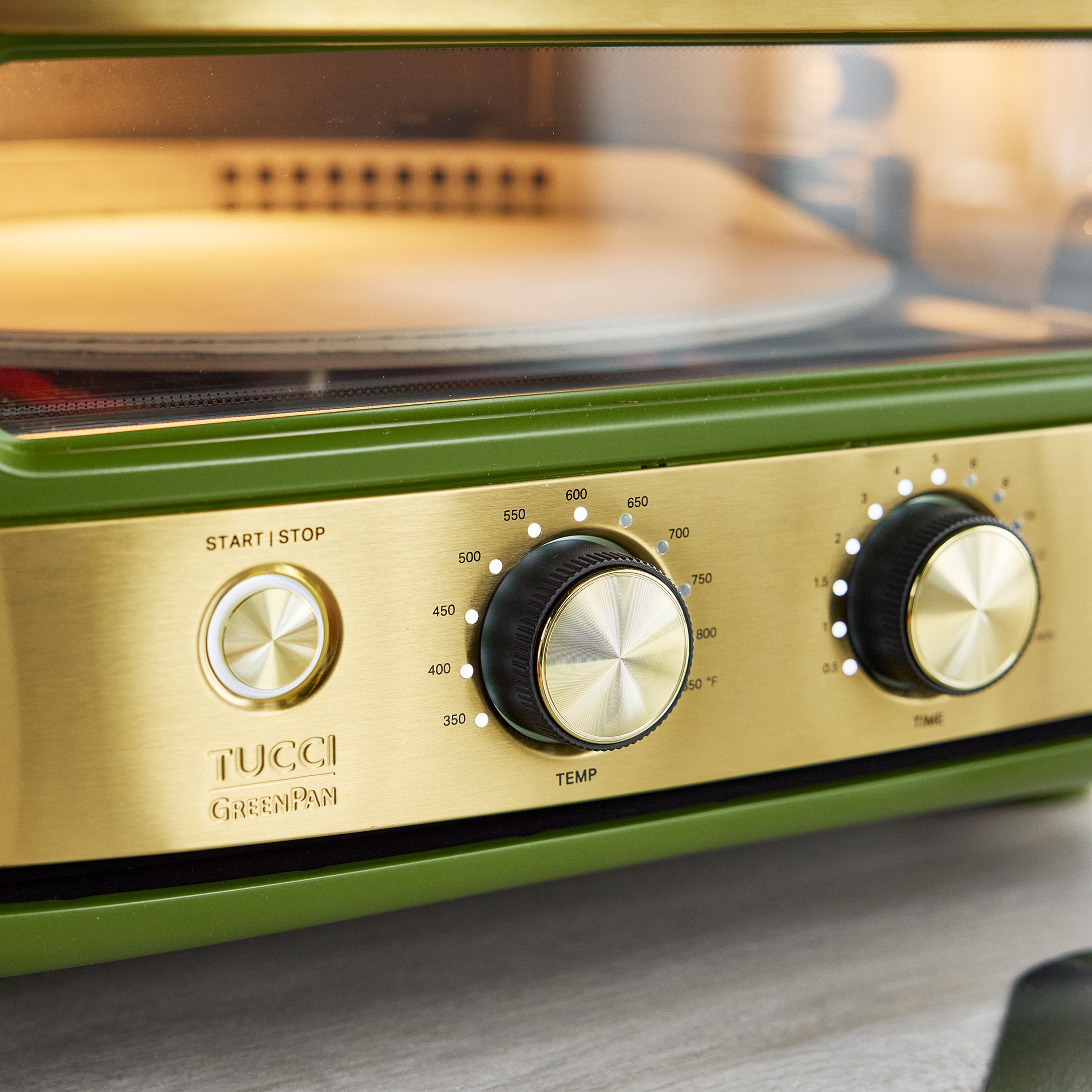 Close-up of a green and gold pizza oven with control knobs on a blurred background