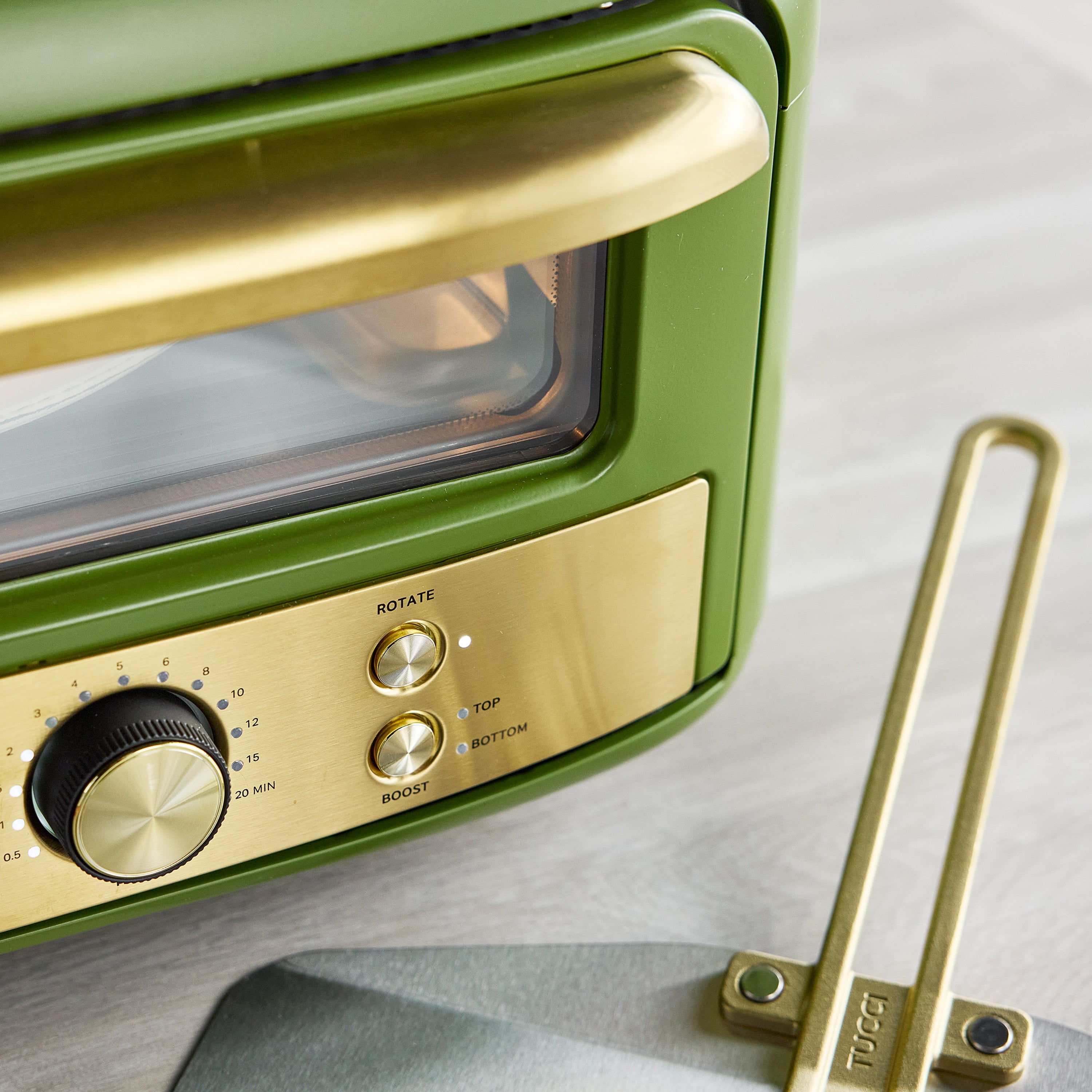Green and gold pizza oven with a pizza peel on a light gray background