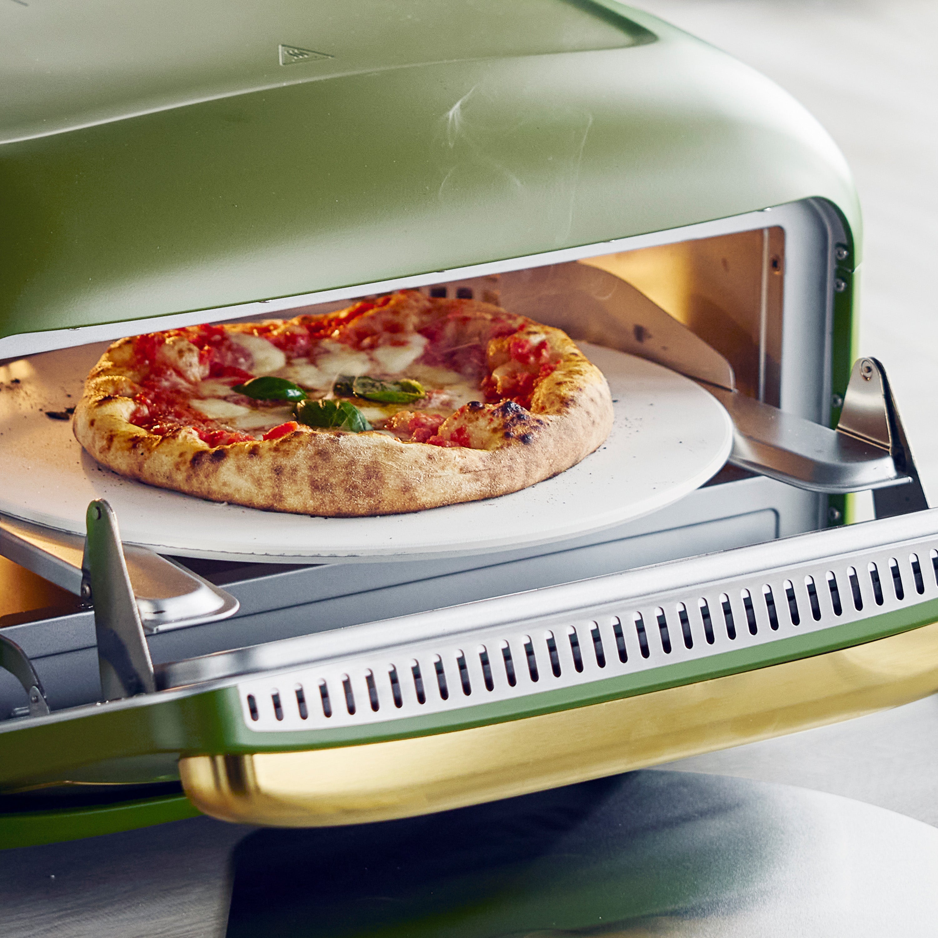 Pizza being cooked in a pizza oven with a green exterior.