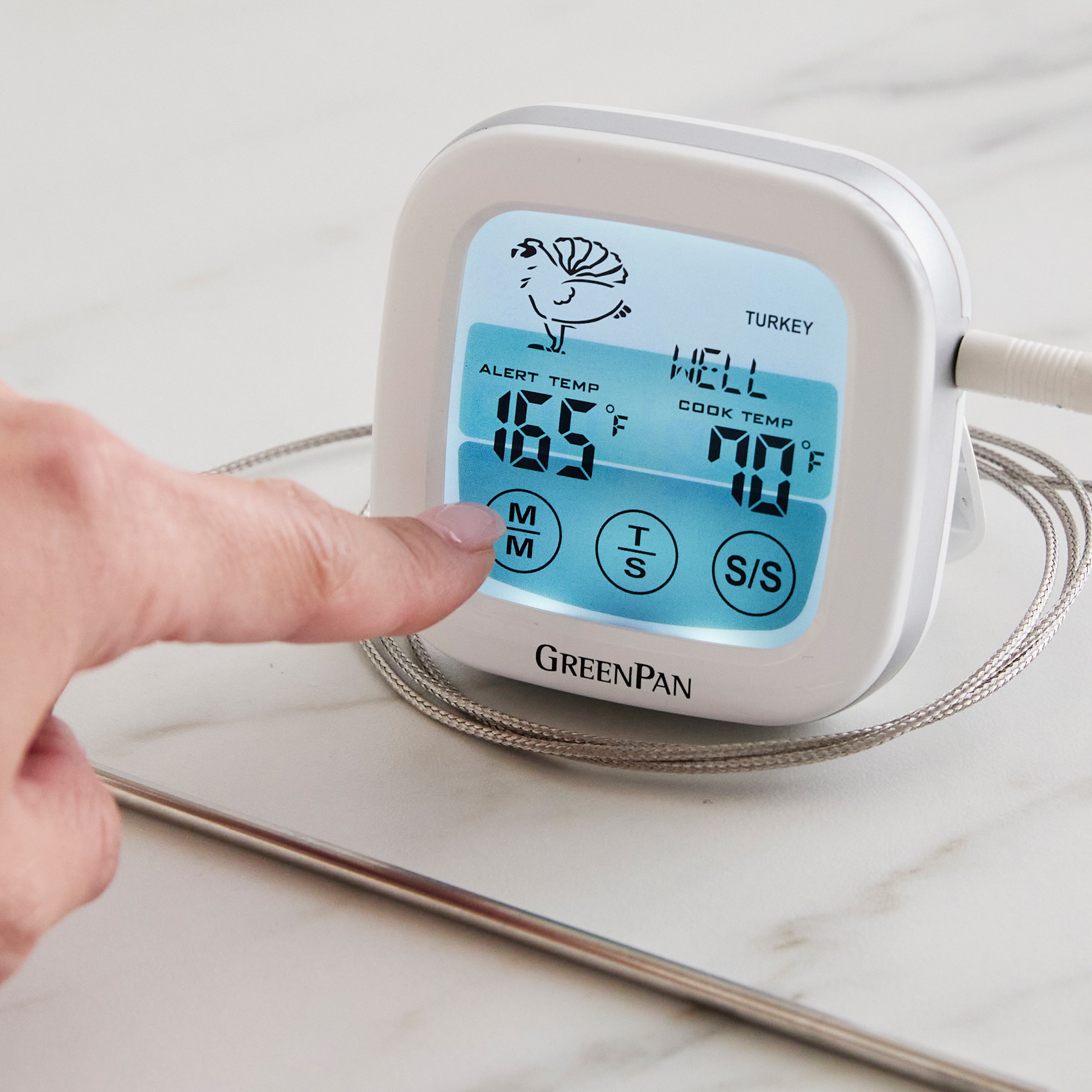 A hand presses a digital oven thermometer displaying turkey temperature on a marble countertop.