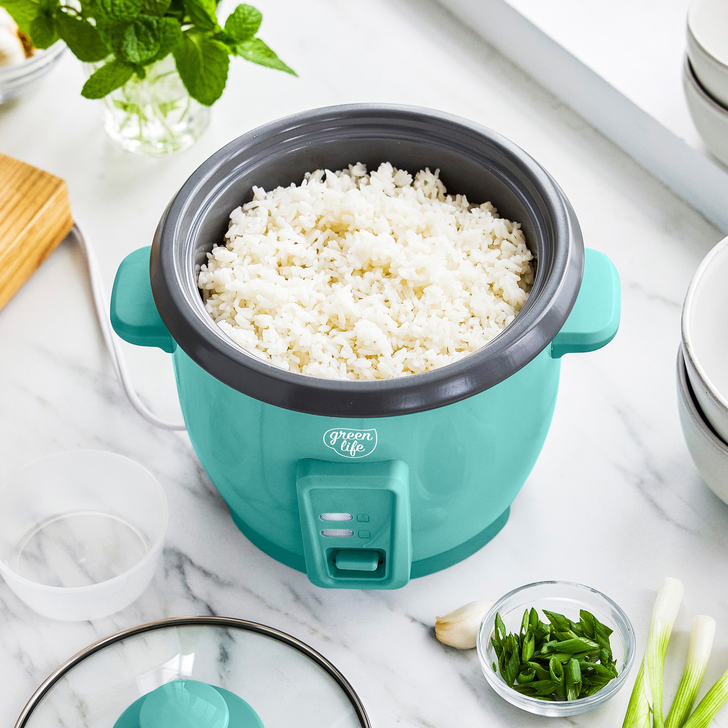 Turquoise rice cooker with white rice on a marble countertop with green onions and garlic.