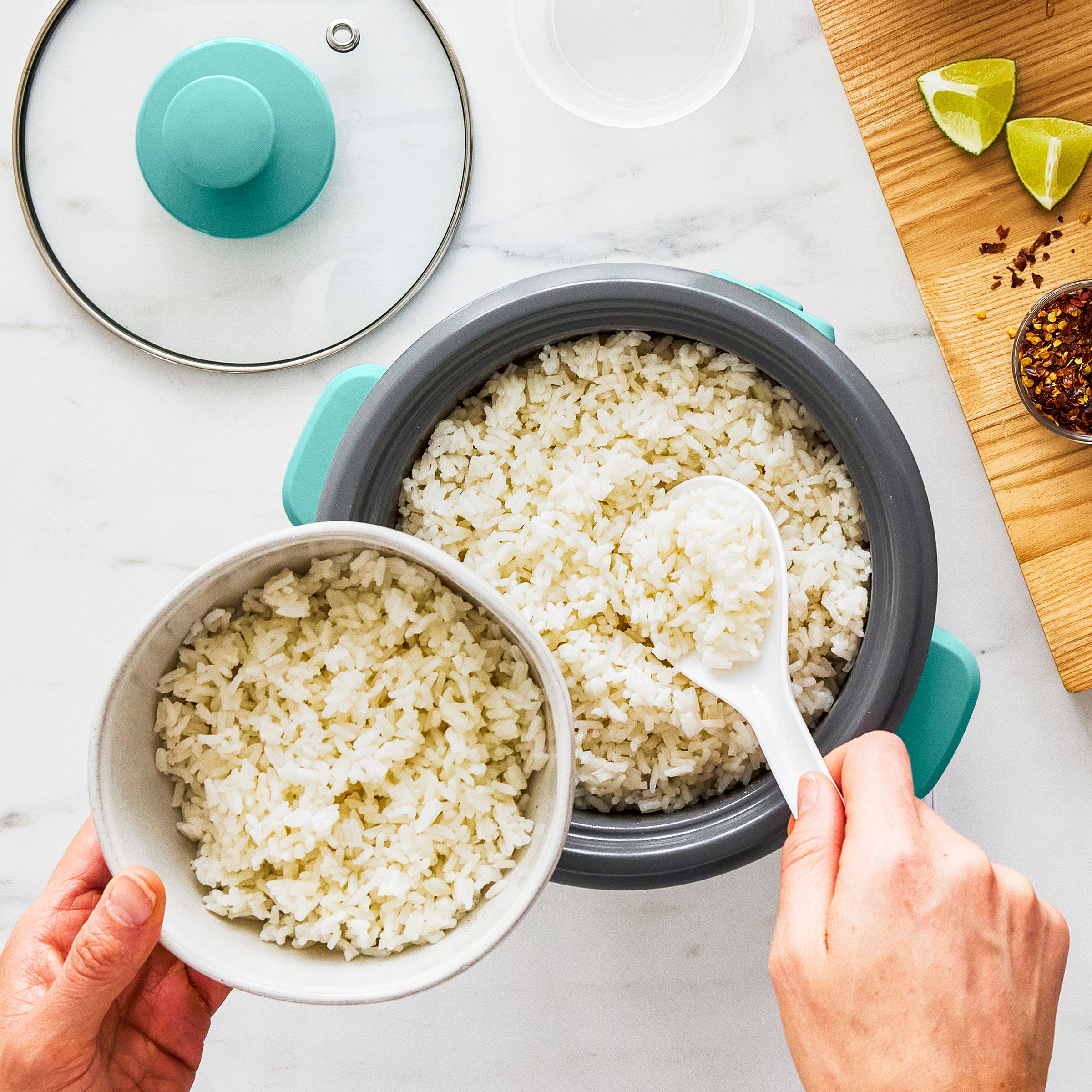 Person serving rice from a rice cooker into a bowl on a white surface.