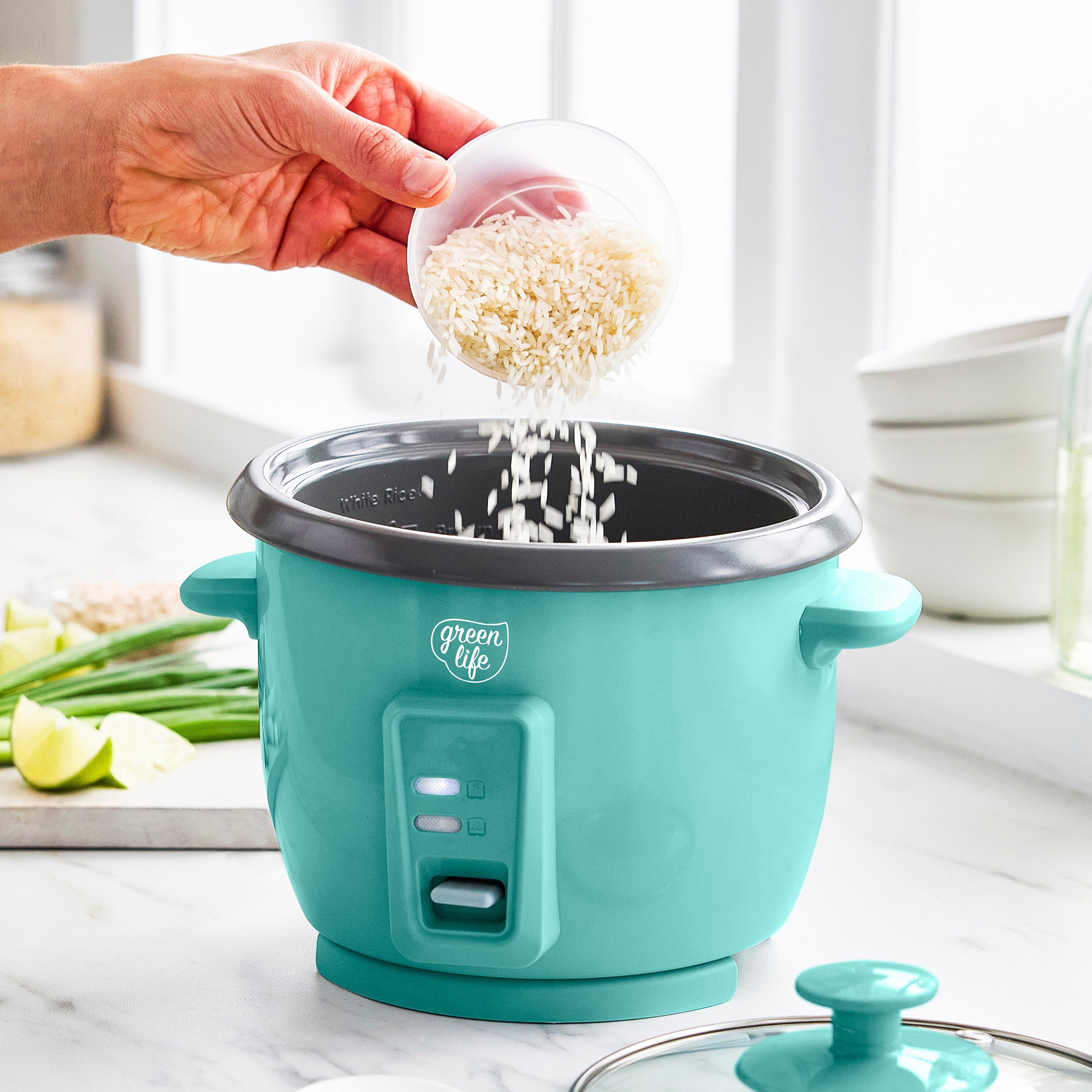 Turquoise rice cooker with a person adding rice, set against a kitchen background.