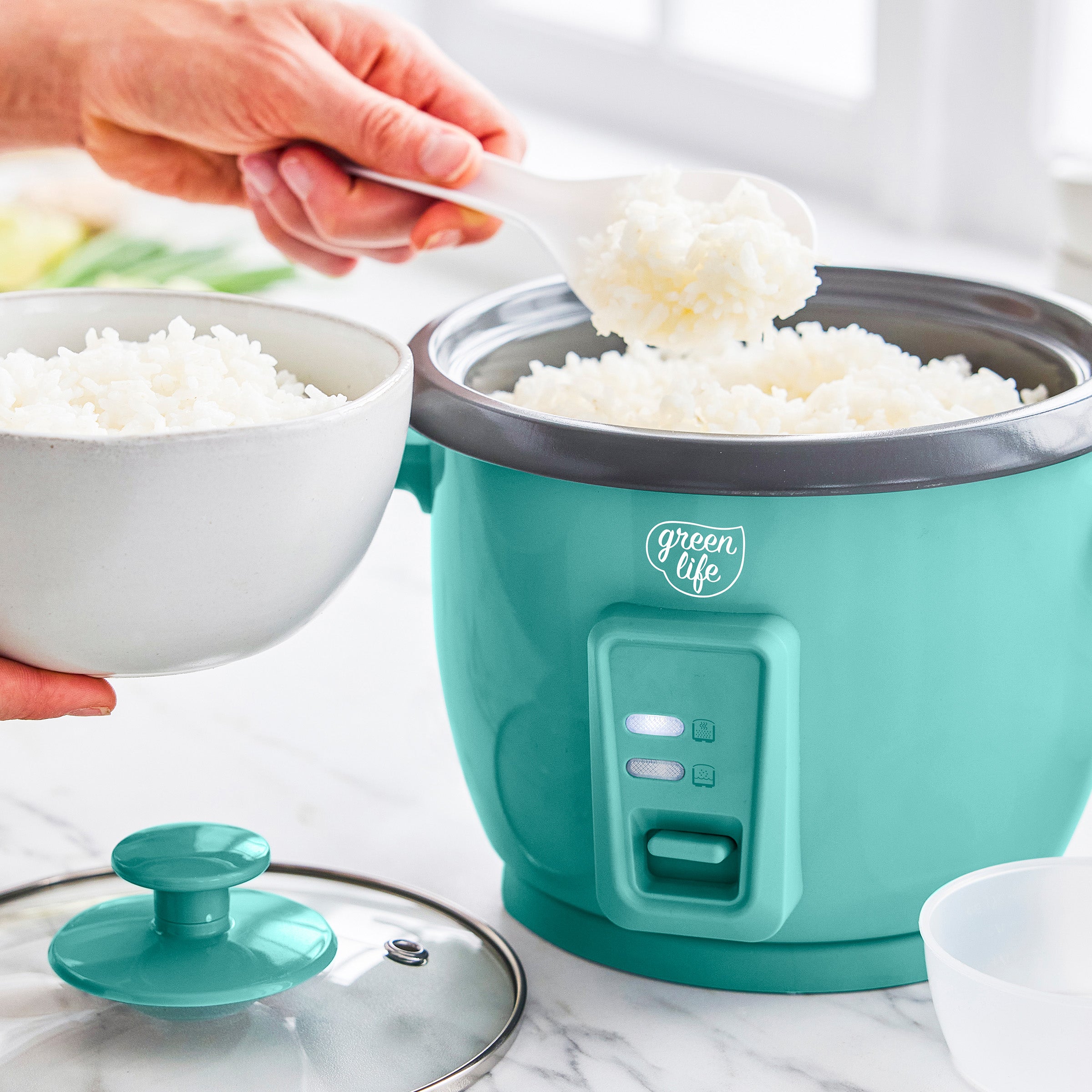 Turquoise rice cooker with white rice being poured into a bowl on a marble surface.