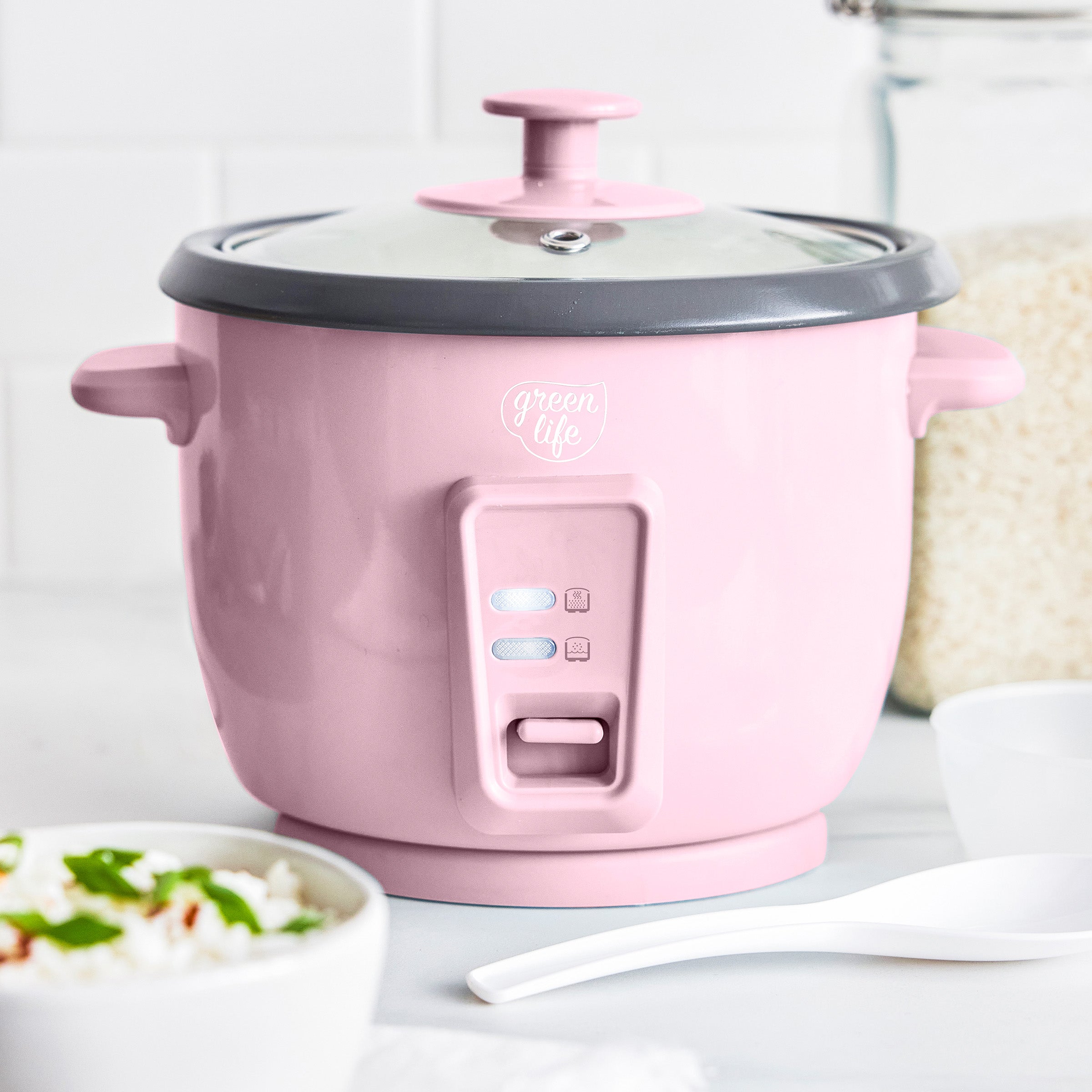 Pink rice cooker with a bowl of rice and a spoon on a white surface