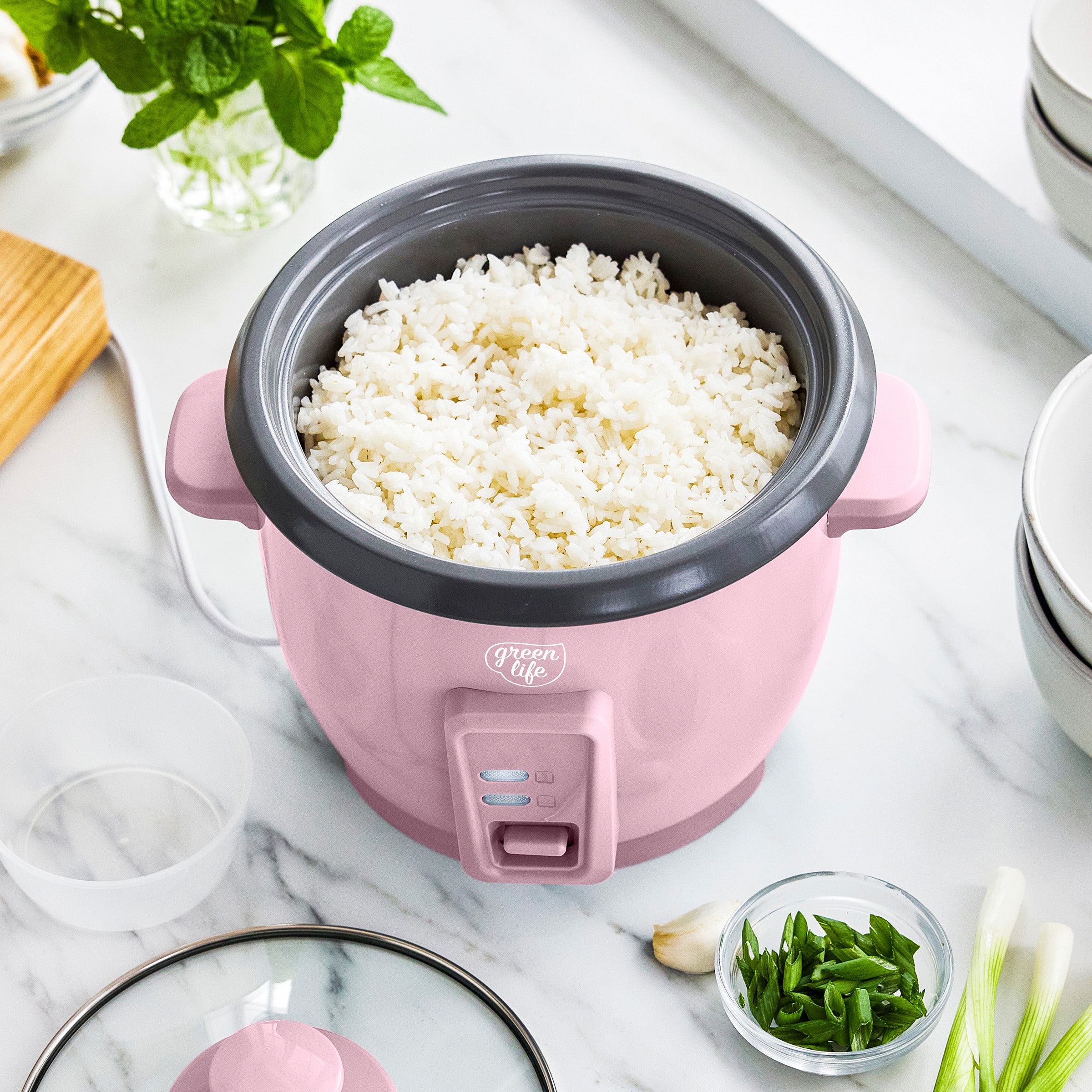 Pink rice cooker with white rice on a marble surface with green onions and garlic.