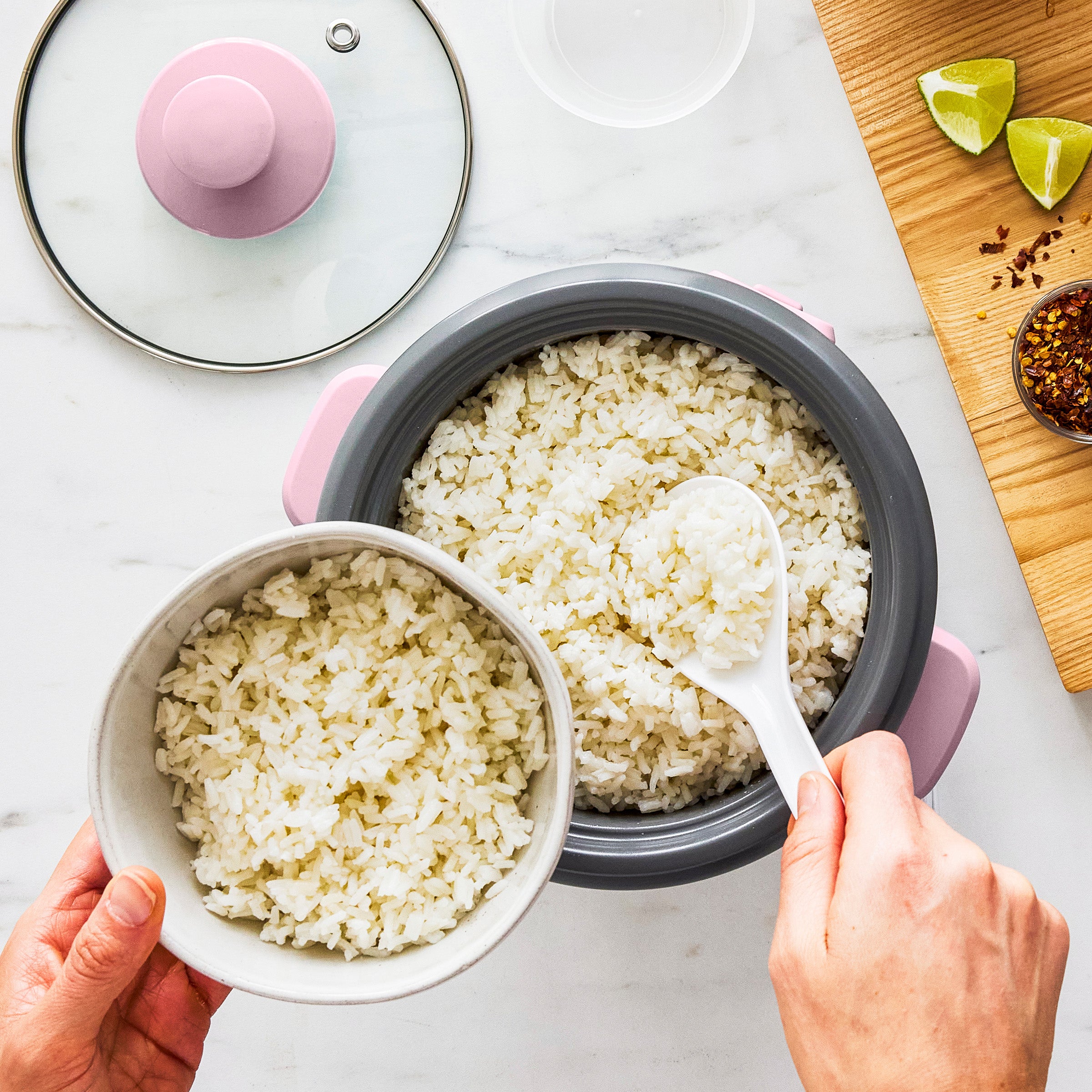 Person serving rice from a rice cooker into a bowl on a light surface.