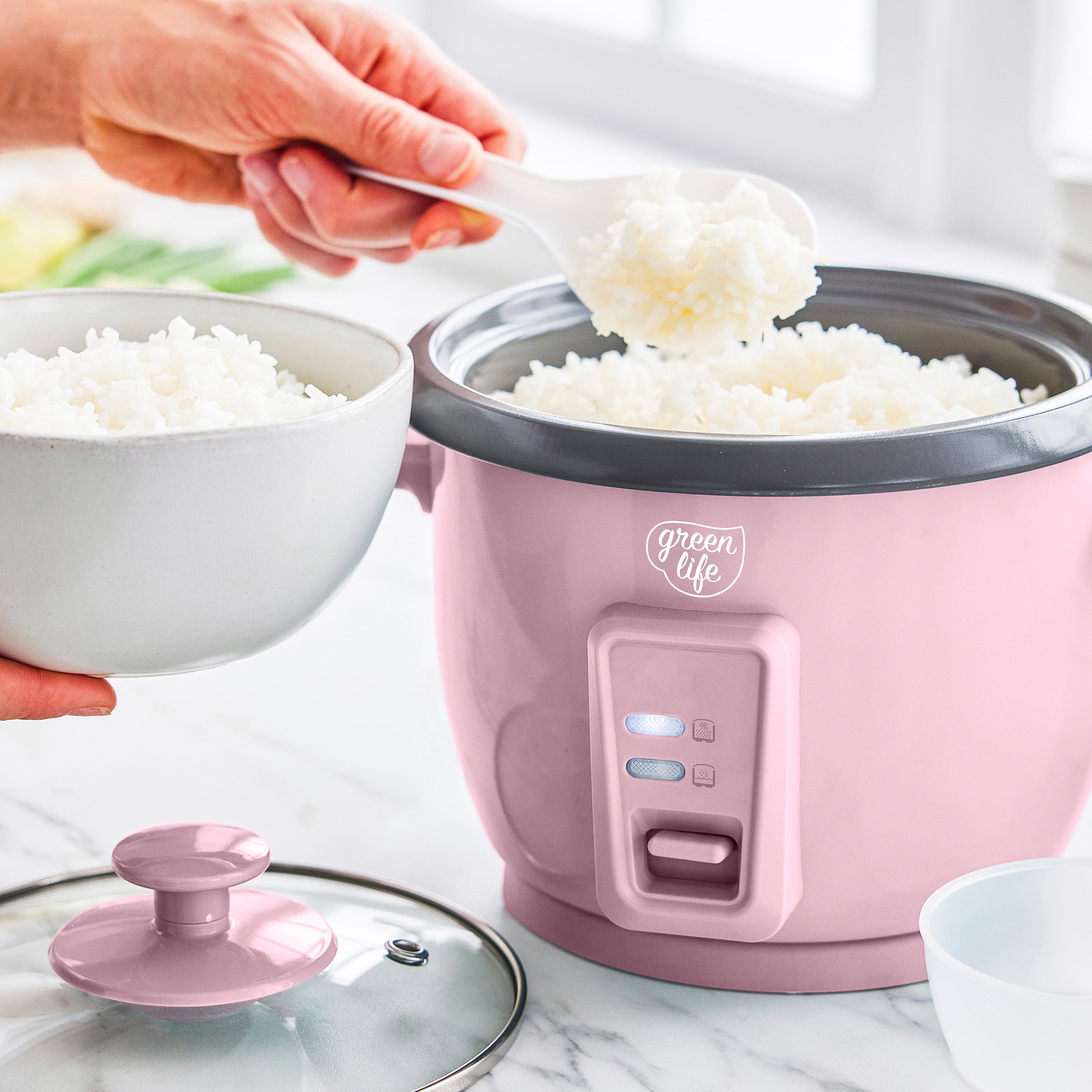 Pink rice cooker with white rice being poured into a bowl, brand 'Green Life' visible.