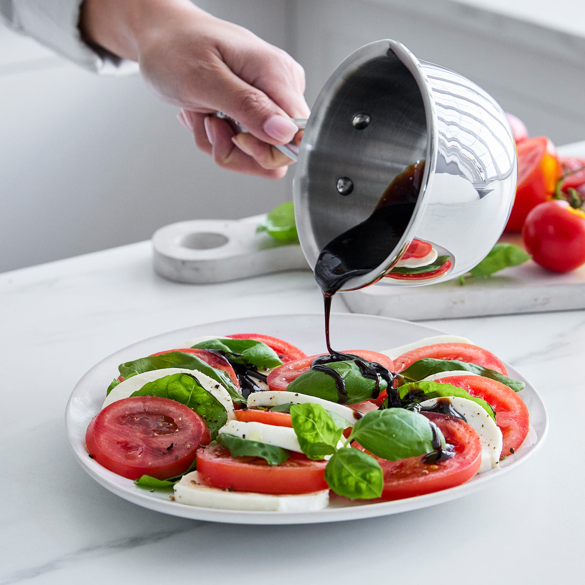 Balsamic glaze being poured over a Caprese salad on a white plate.
