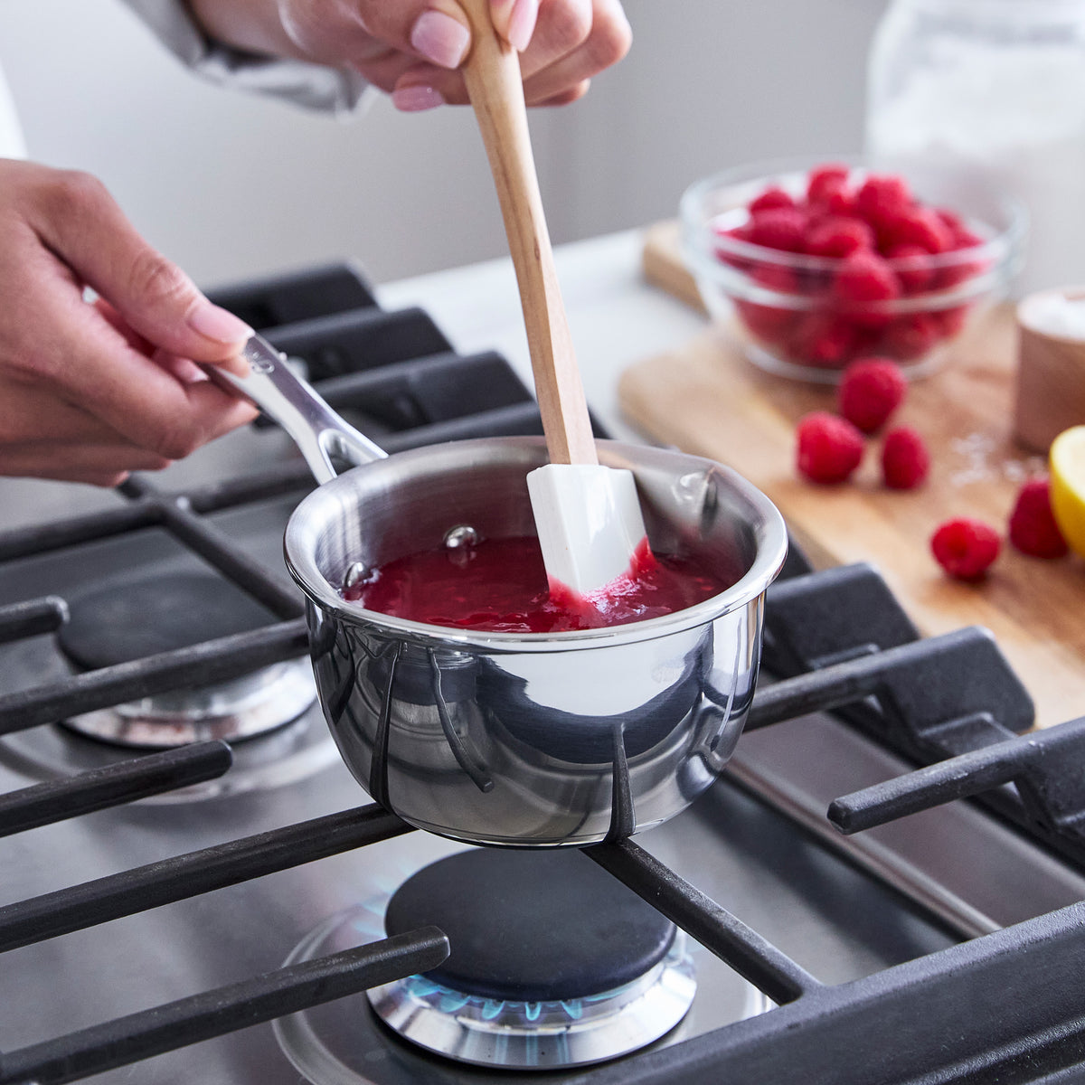 Person stirring a butter warmer on a stove with a wooden spatula.