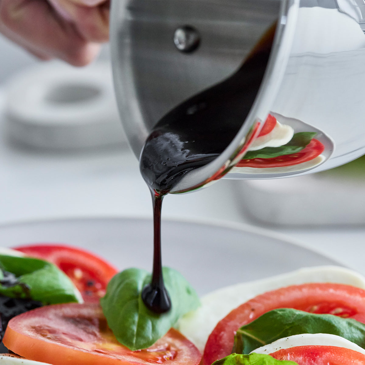 Balsamic glaze being poured over a Caprese salad on a white plate.