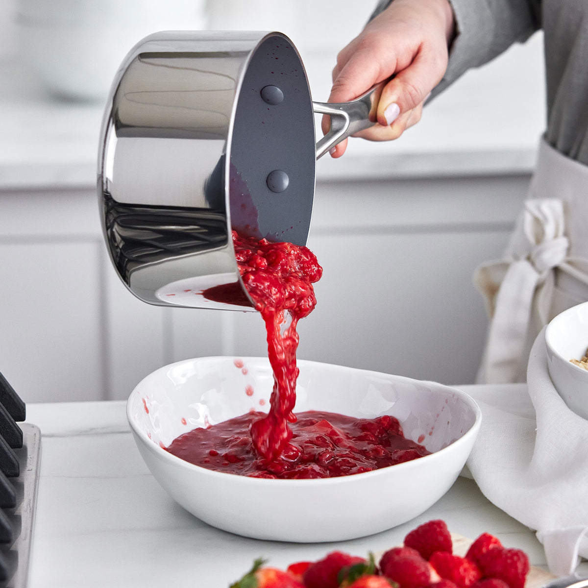 Raspberry sauce being poured from a Valencia Pro Stainless Steel 9-piece saucepan into a white bowl.