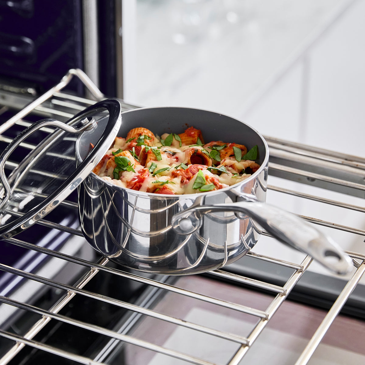 Valencia Pro 9-piece stainless steel saucepan with lid, containing baked pasta with tomato sauce and melted cheese inside an oven.