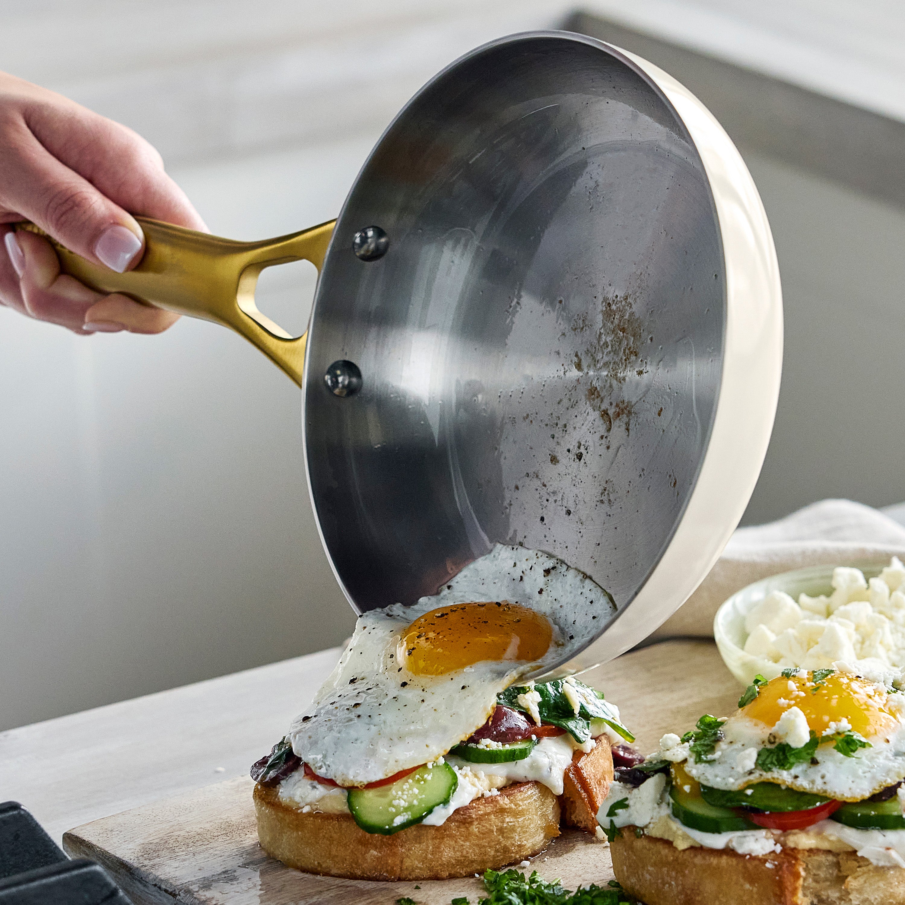 Person pouring a fried egg onto a slice of bread with vegetables on a wooden cutting board.