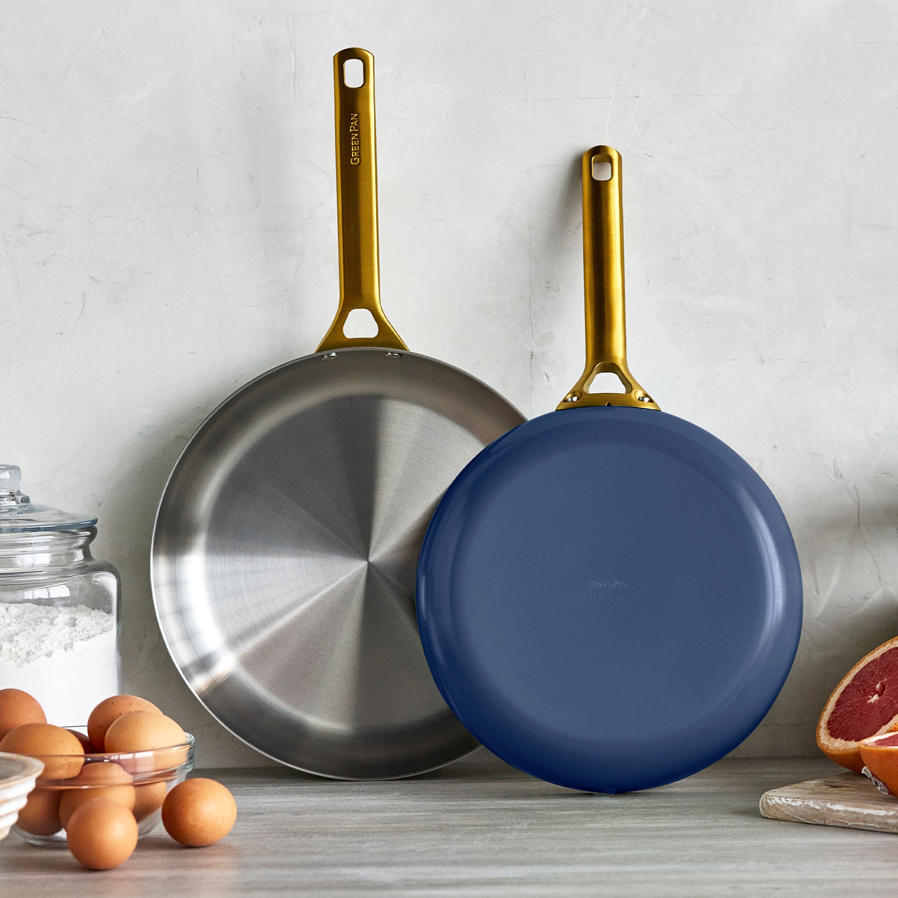 Two frying pans with gold handles on a kitchen counter.