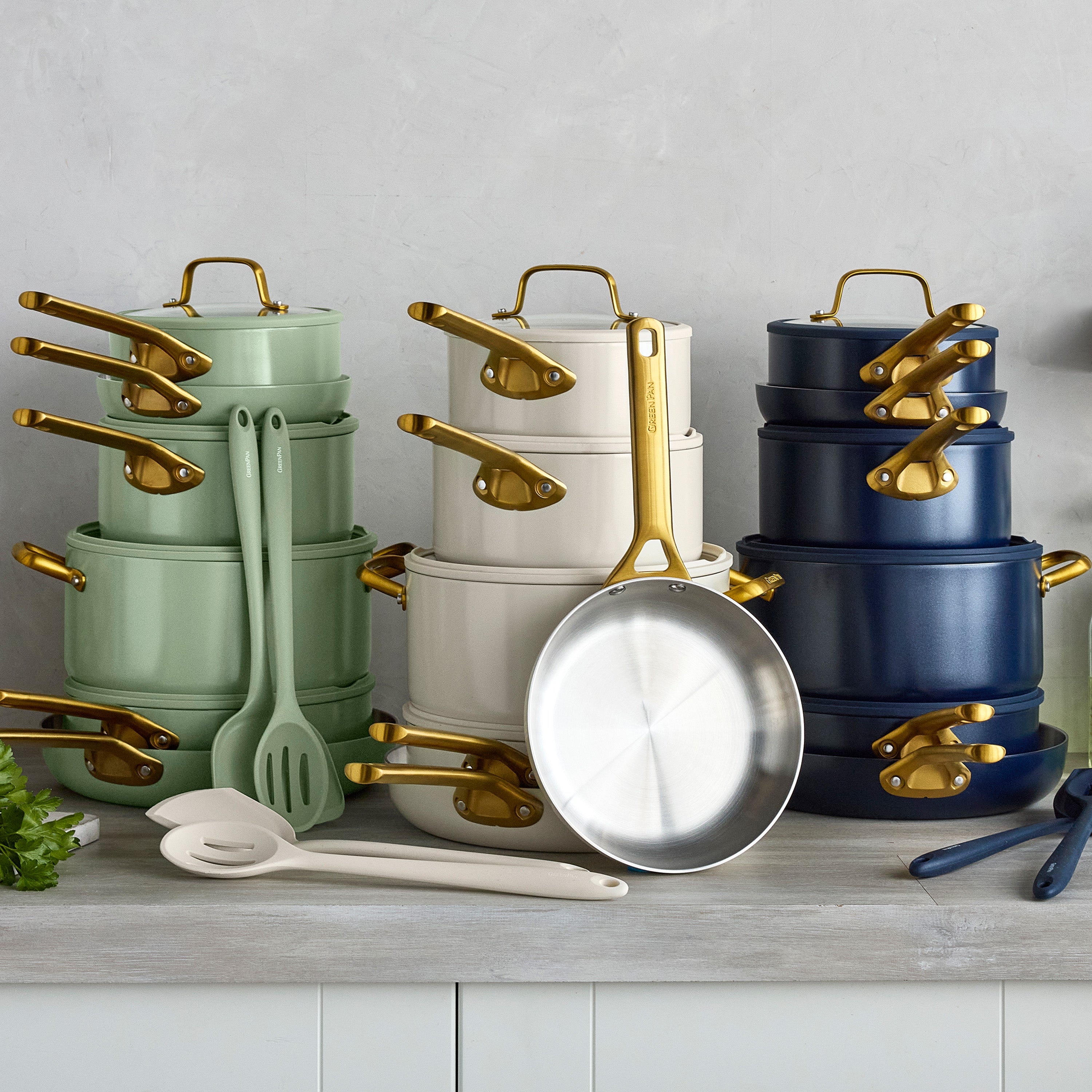 Set of pots, pans, and kitchen utensils with gold handles on a gray surface.