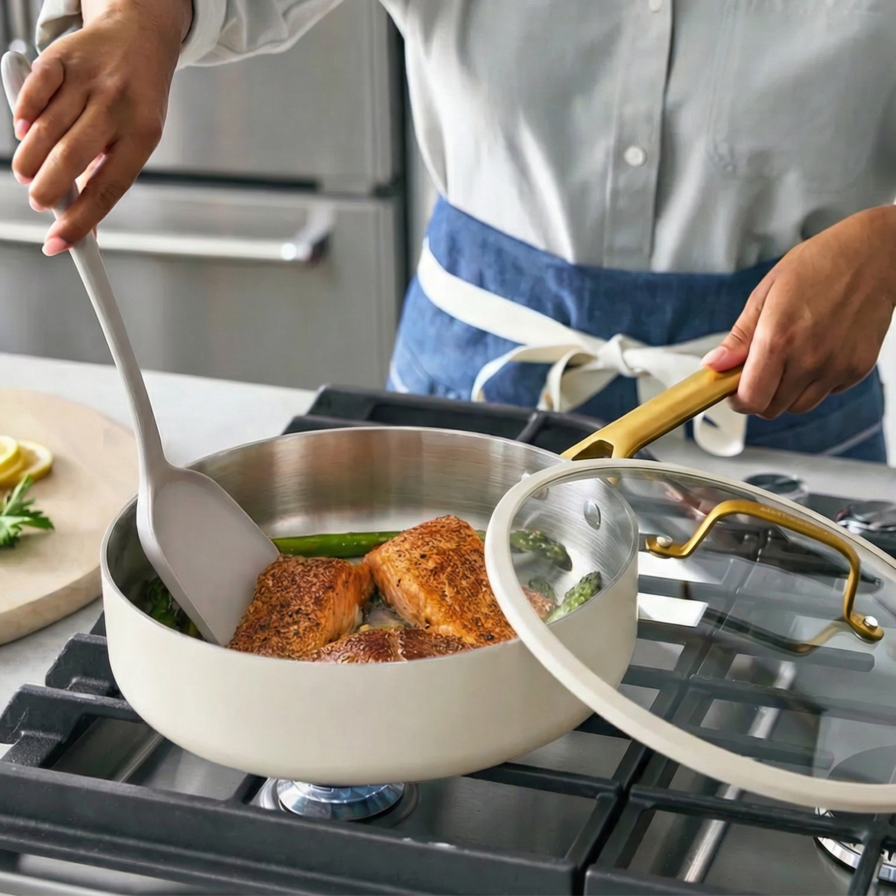 Person cooking salmon in a pan on a stove with a lid in hand