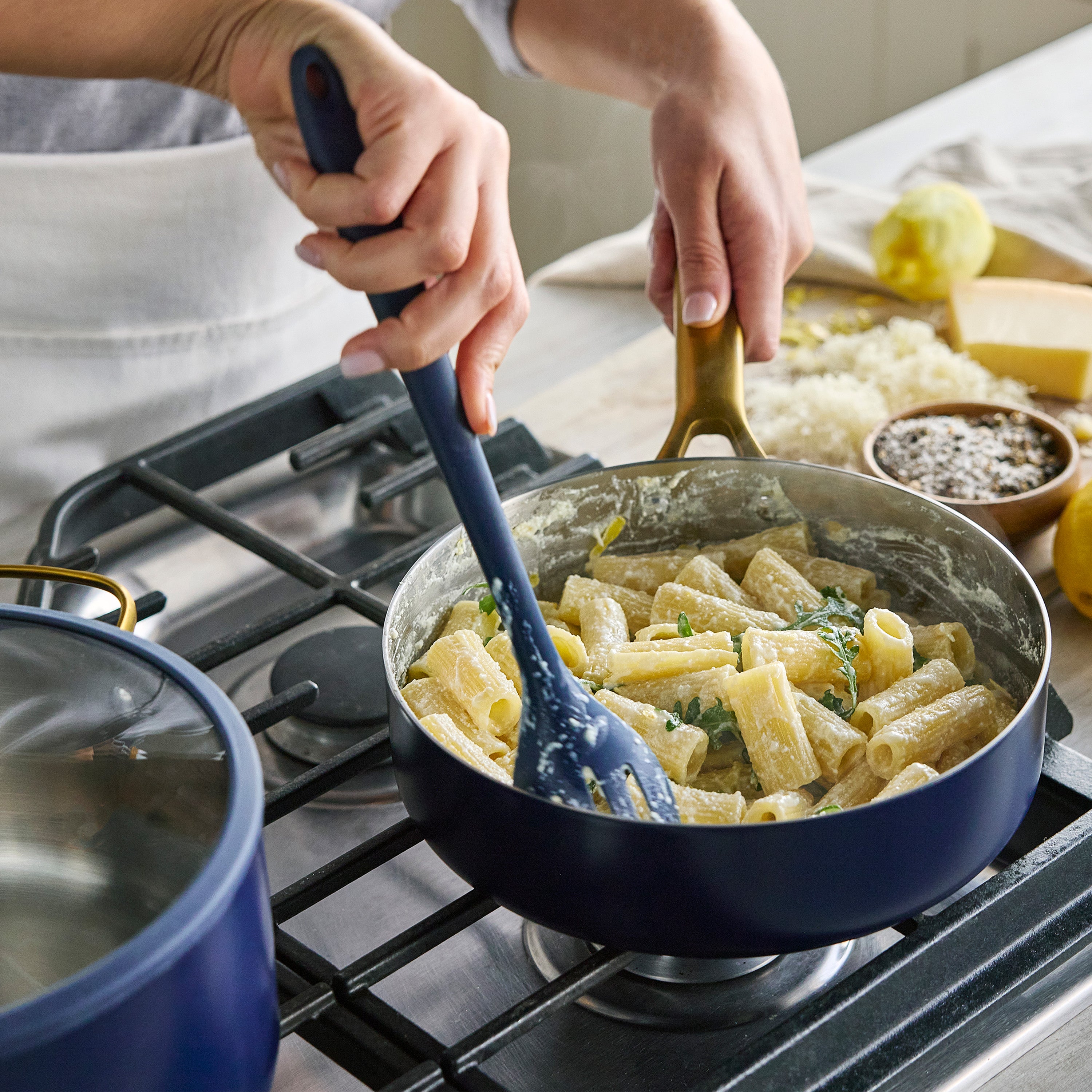 Person cooking pasta in a pan on a stove with a blue spoon.