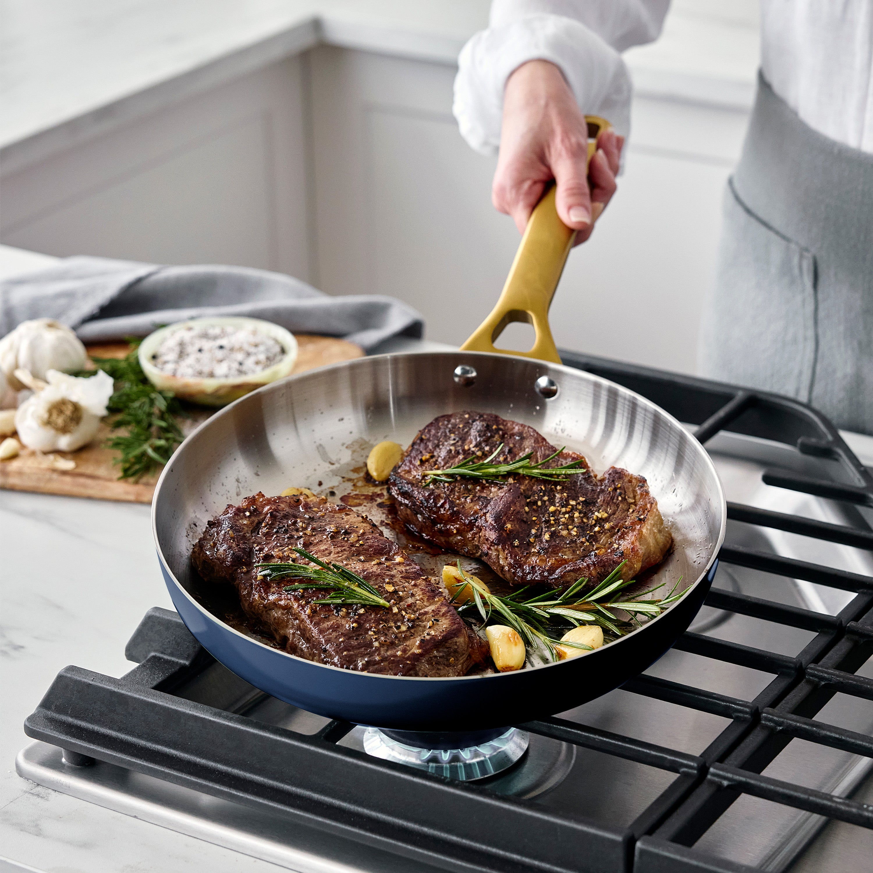 Steaks being cooked in a pan on a stove with a person holding the handle.