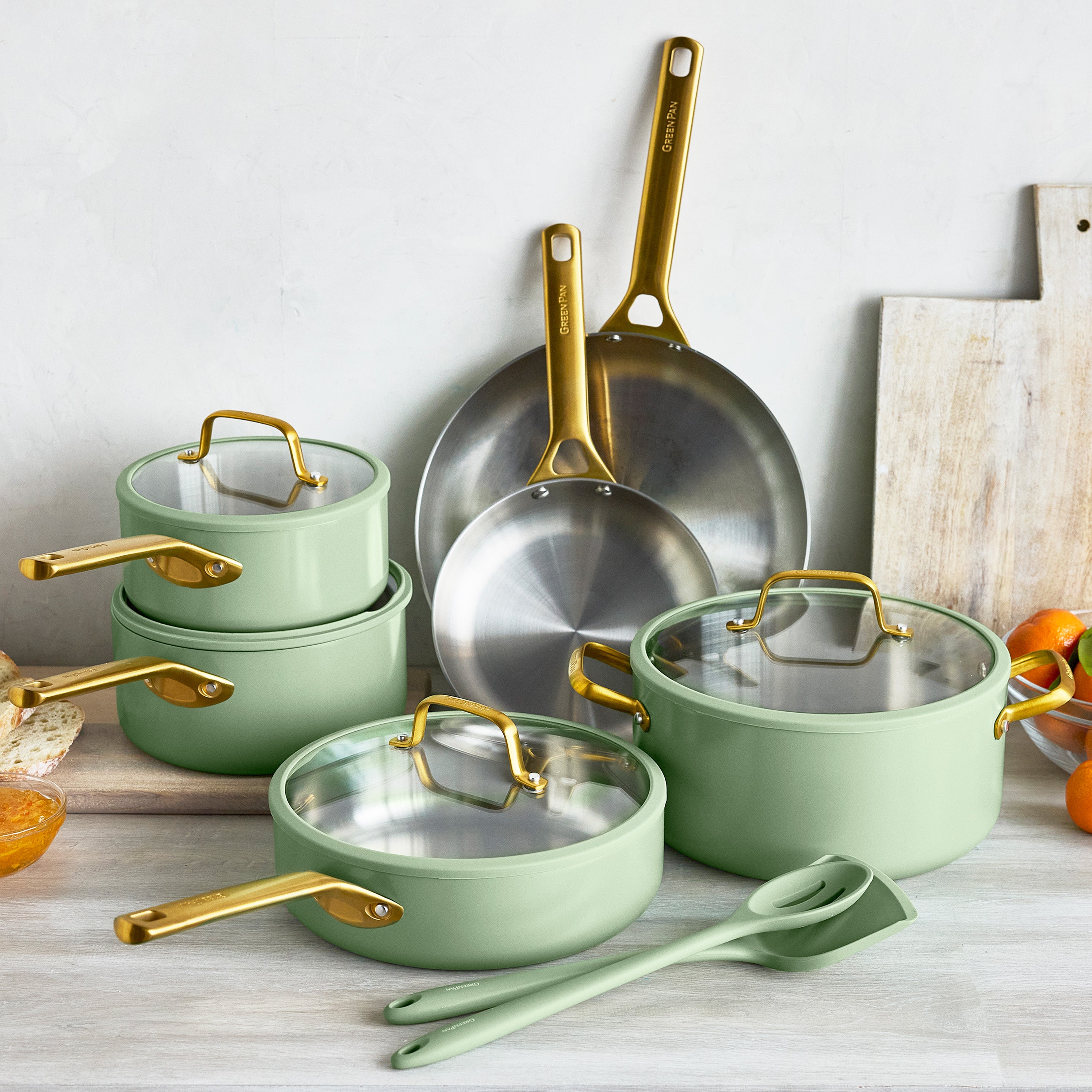 Set of green cookware with gold handles on a light wooden surface.