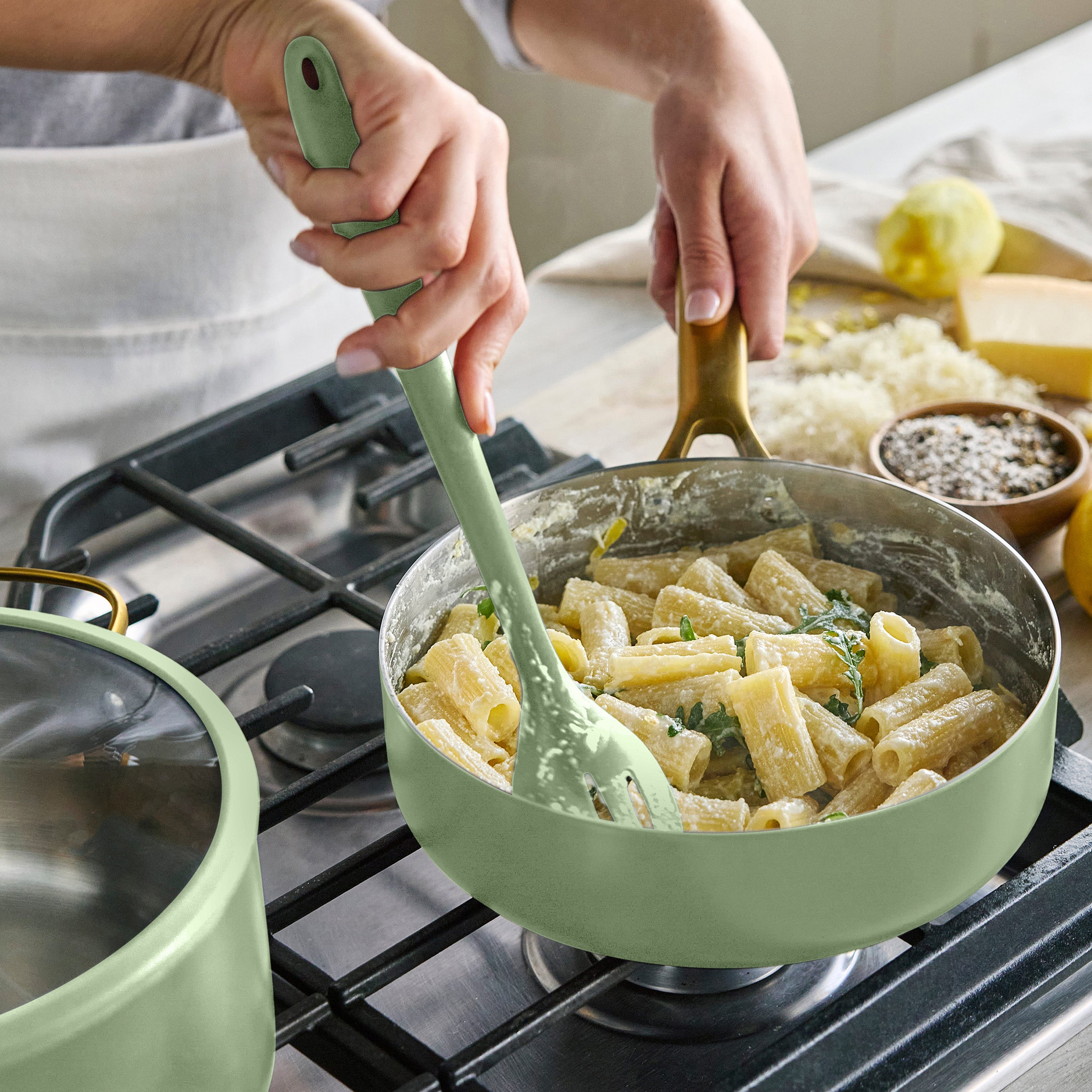 Person cooking pasta in a green pan on a stove with a green spoon.