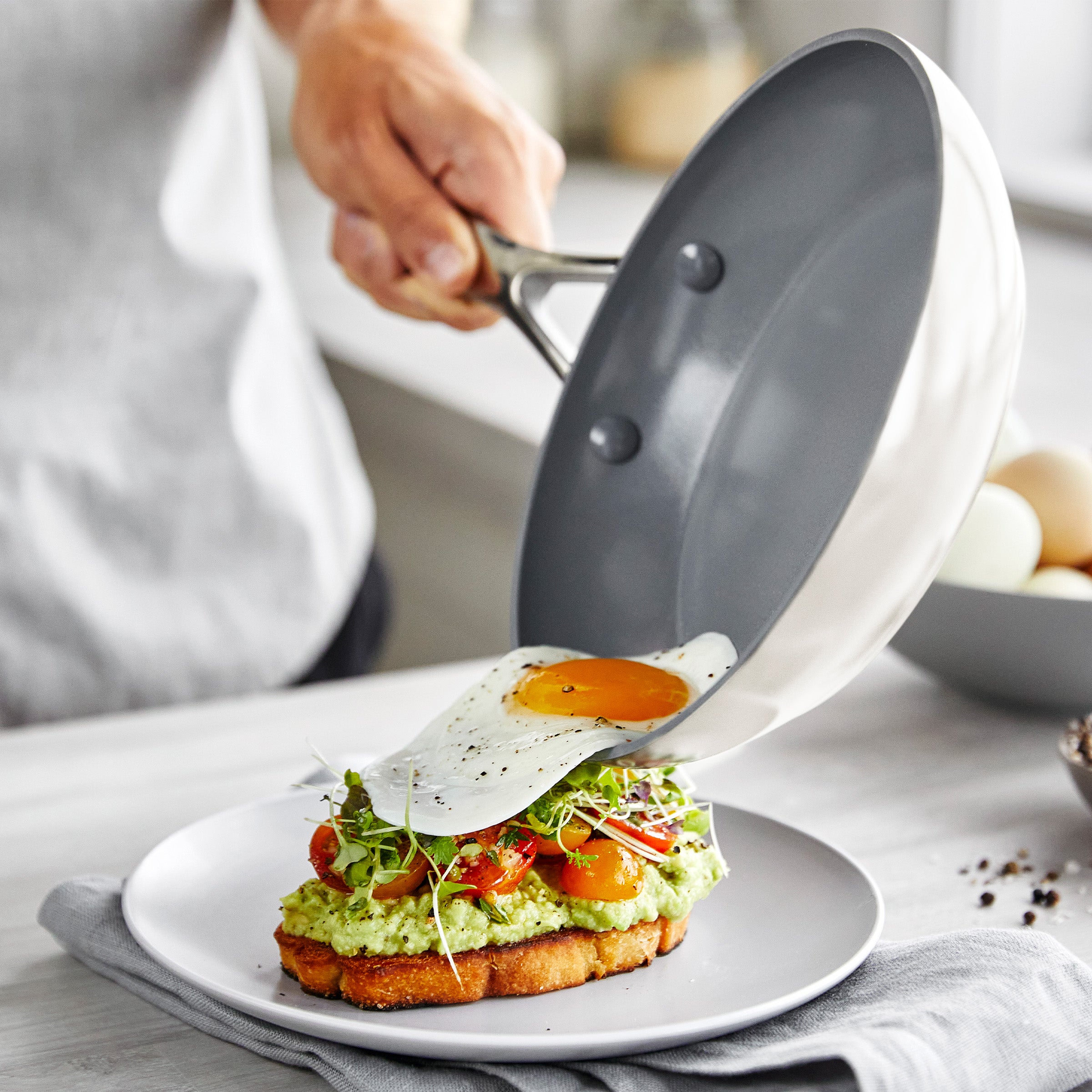 Person sliding a fried egg from a frypan onto avocado toast