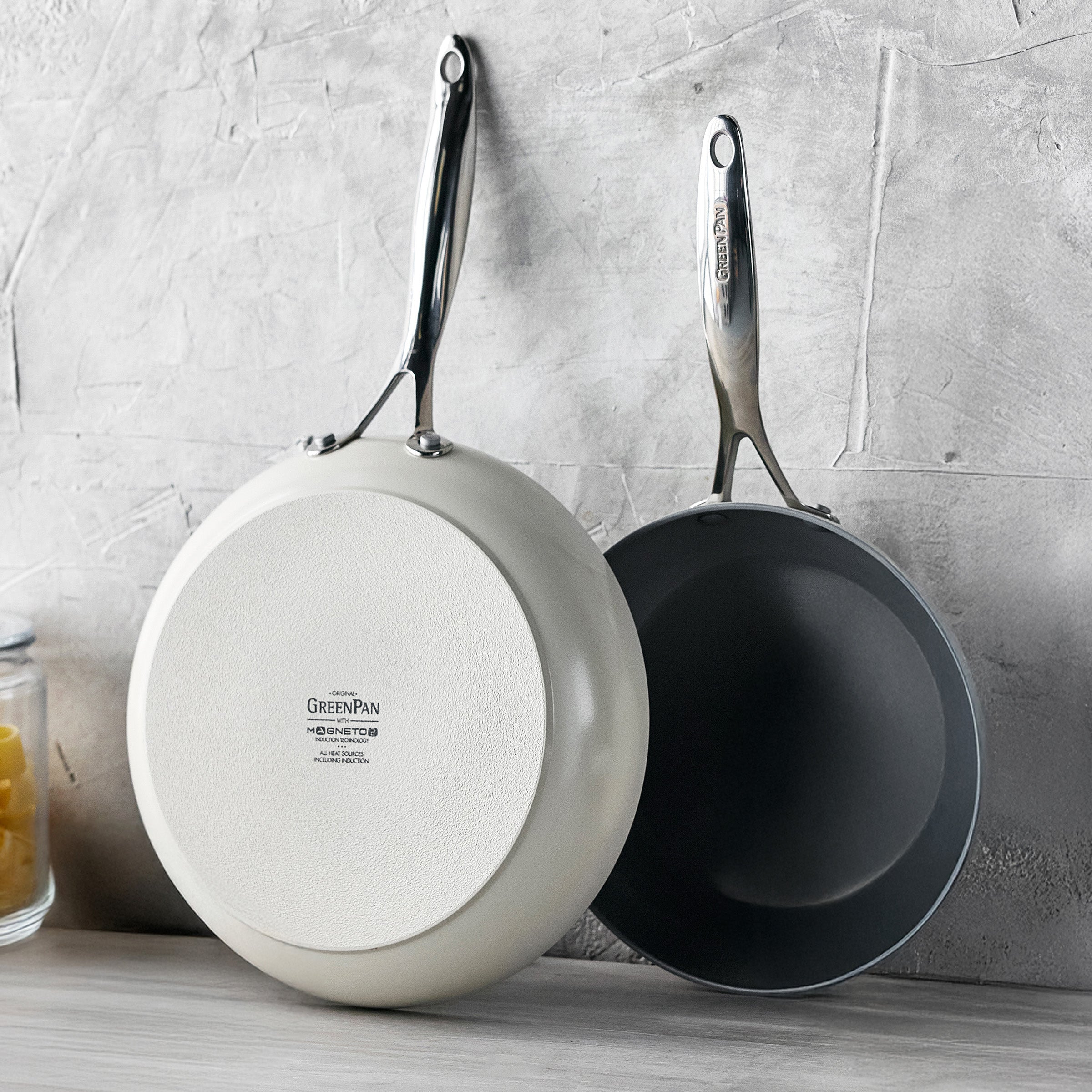 Two frying pans hanging on a textured wall.