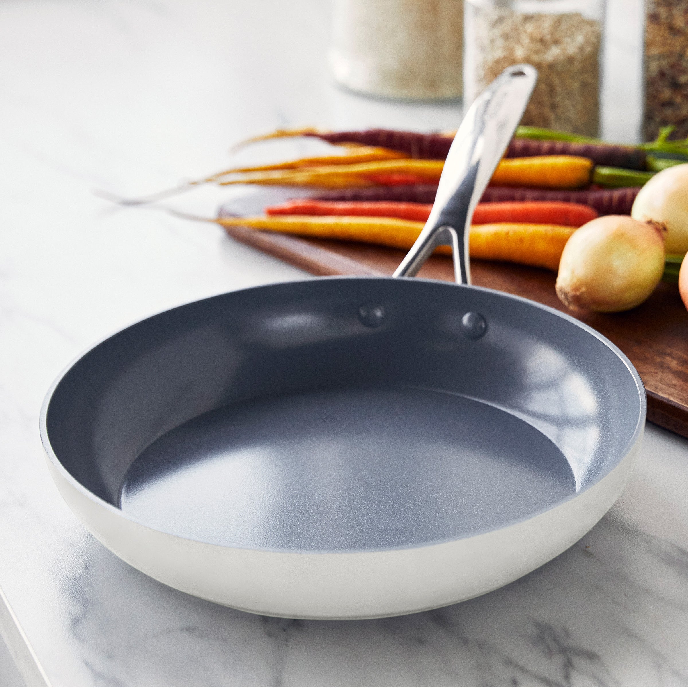 Cream frying pan on a marble surface with vegetables in the background