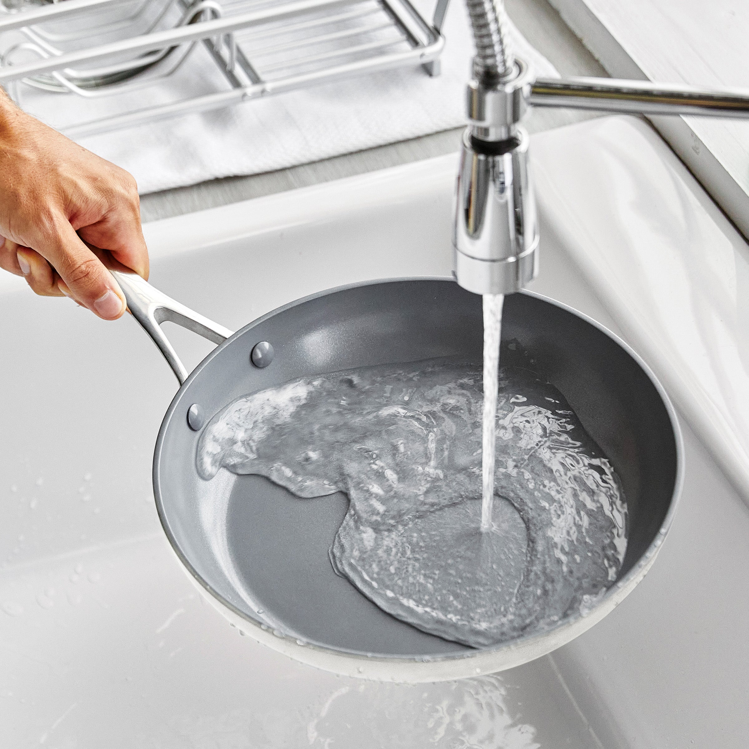 Person washing a frying pan under running water in a kitchen sink.