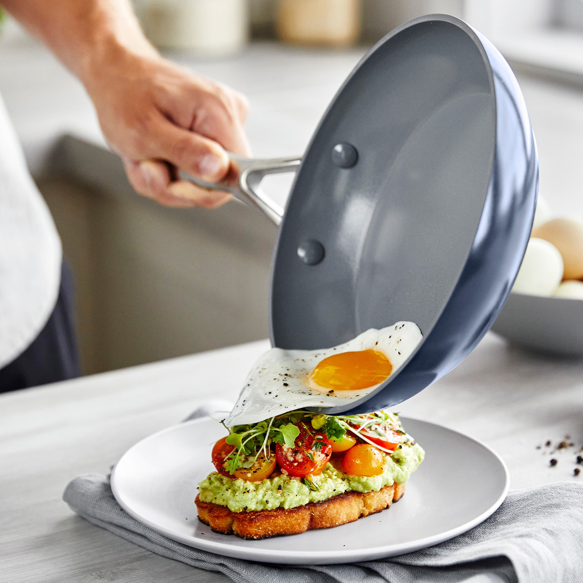 Person sliding a fried egg from a frypan onto avocado toast