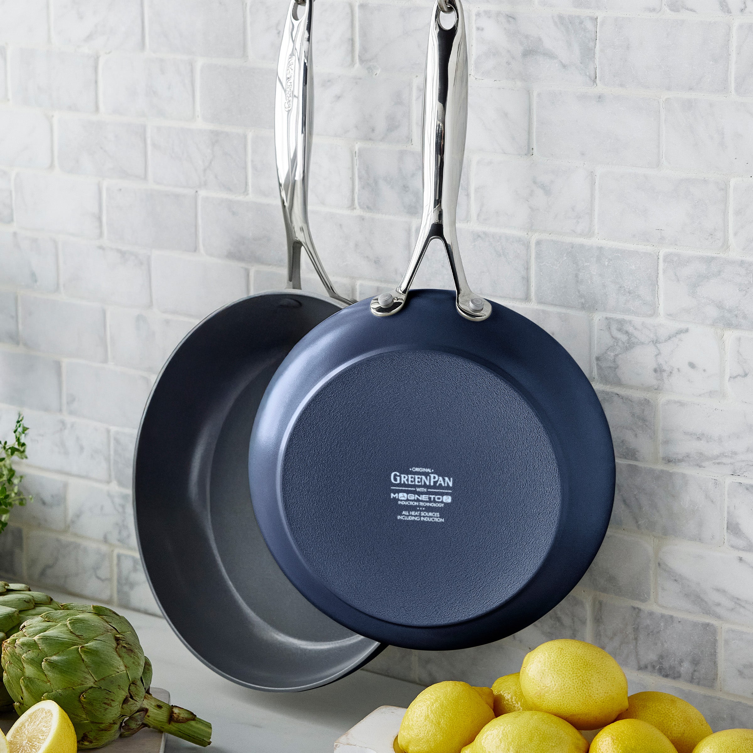 Two frying pans hanging on a textured wall.