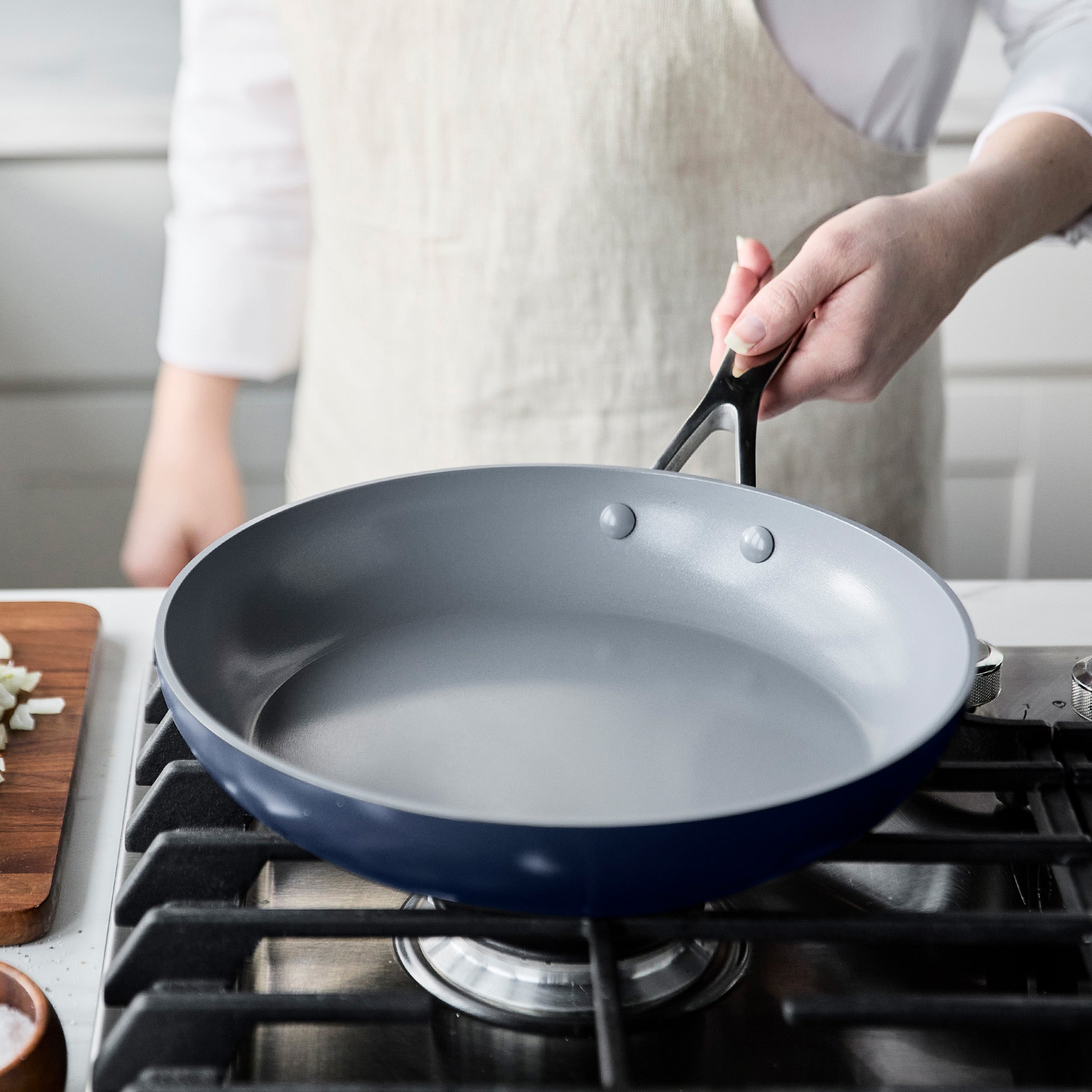 Person holding a blue frying pan over a gas stove