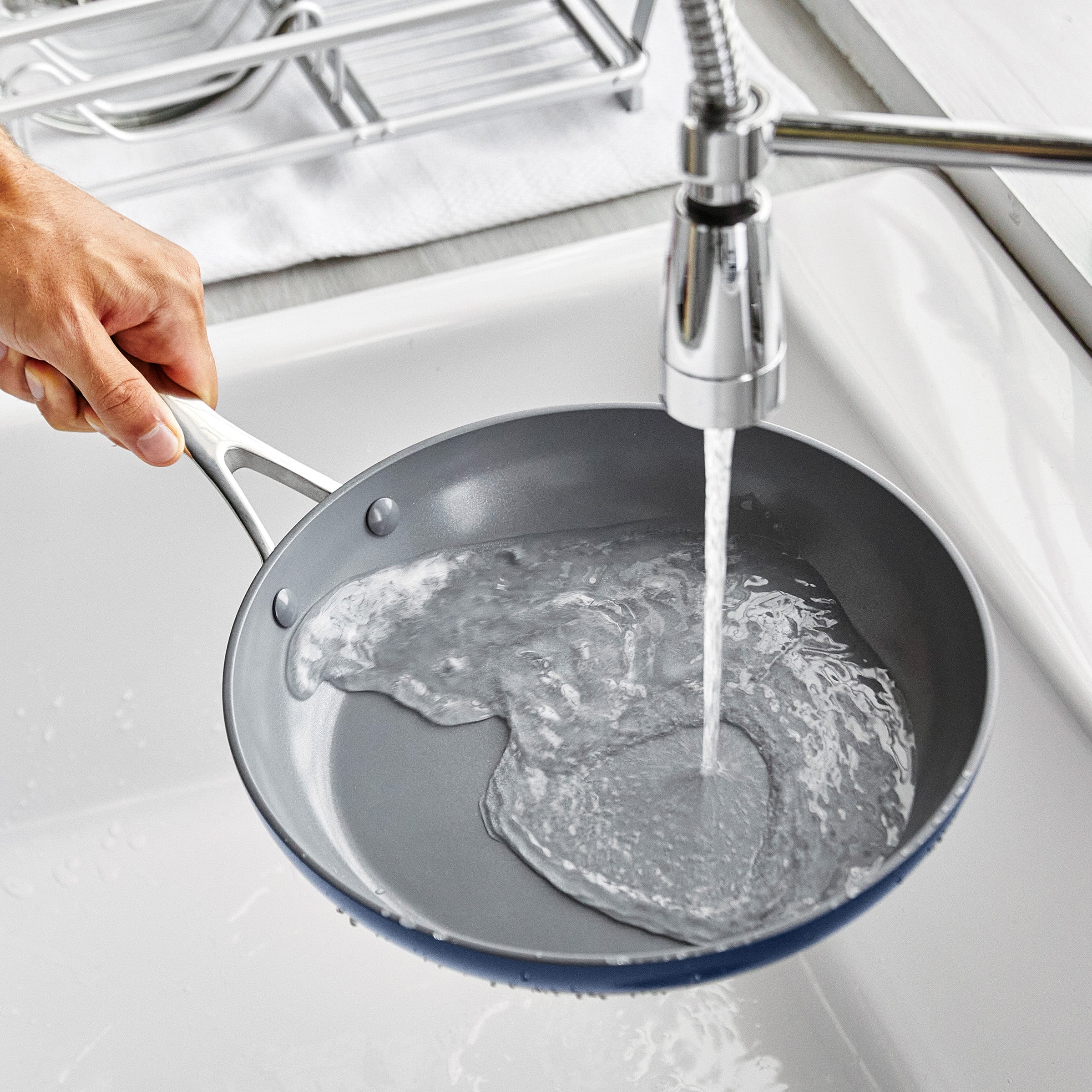 Person washing a frying pan under running water in a kitchen sink.