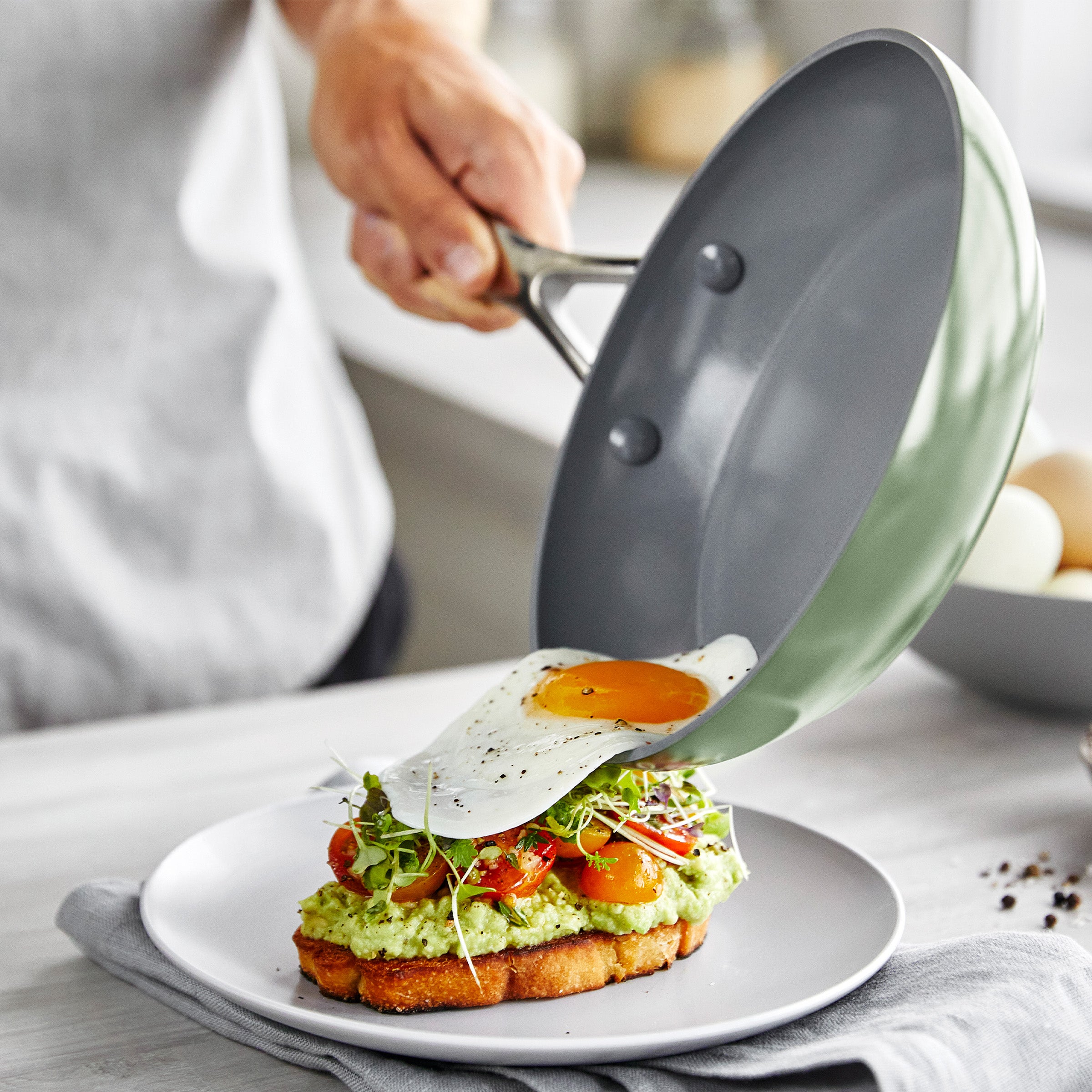 Person sliding a fried egg from a frypan onto avocado toast