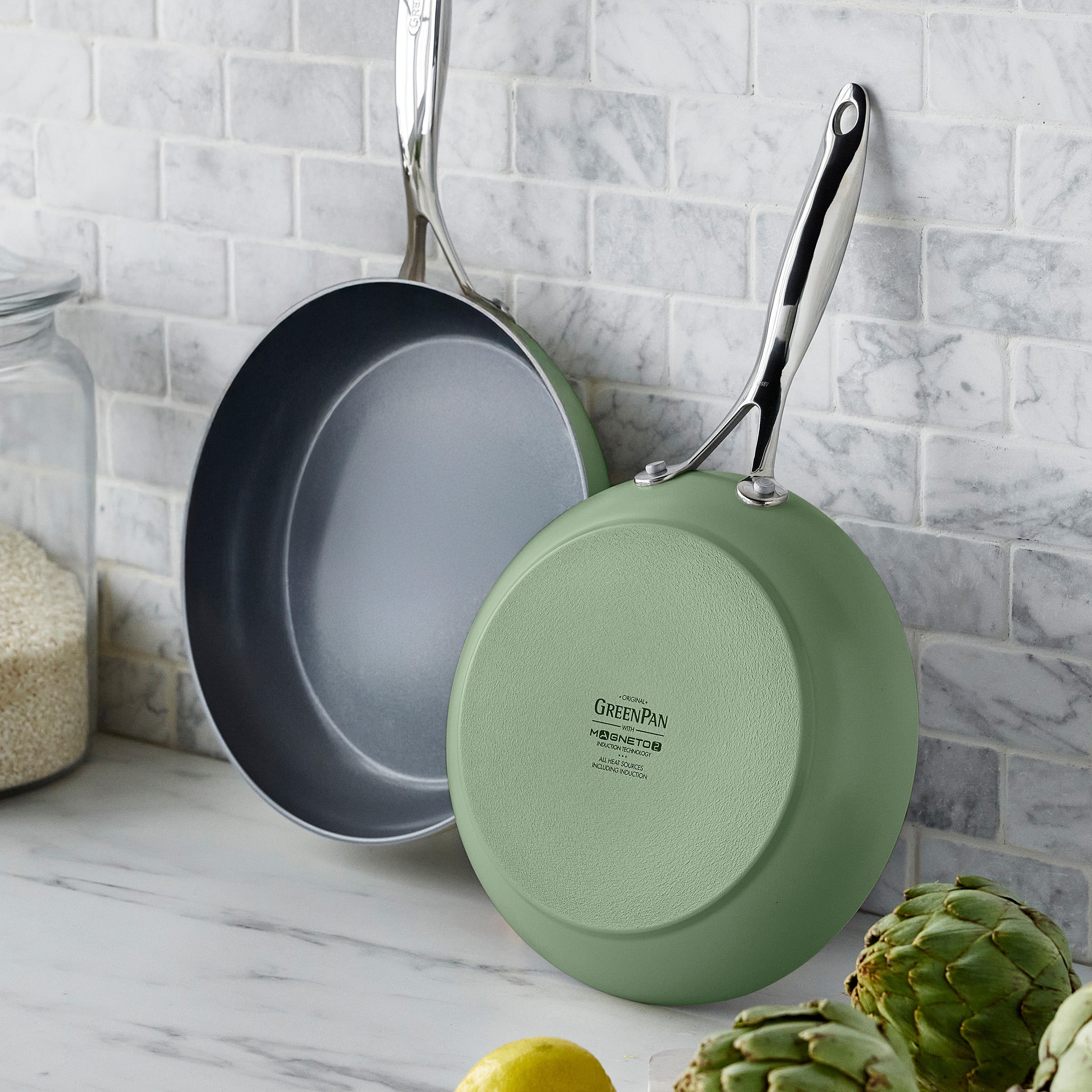Two frying pans hanging on a textured wall.