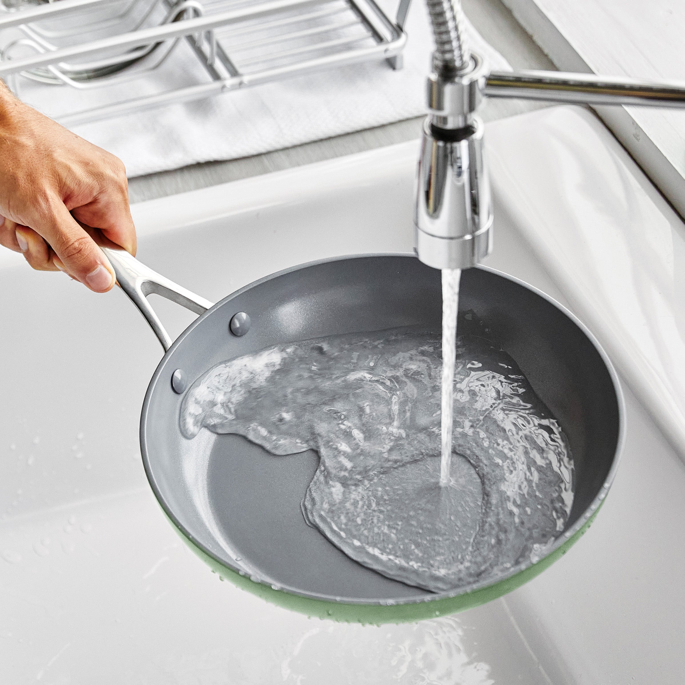 Person washing a frying pan under running water in a kitchen sink.
