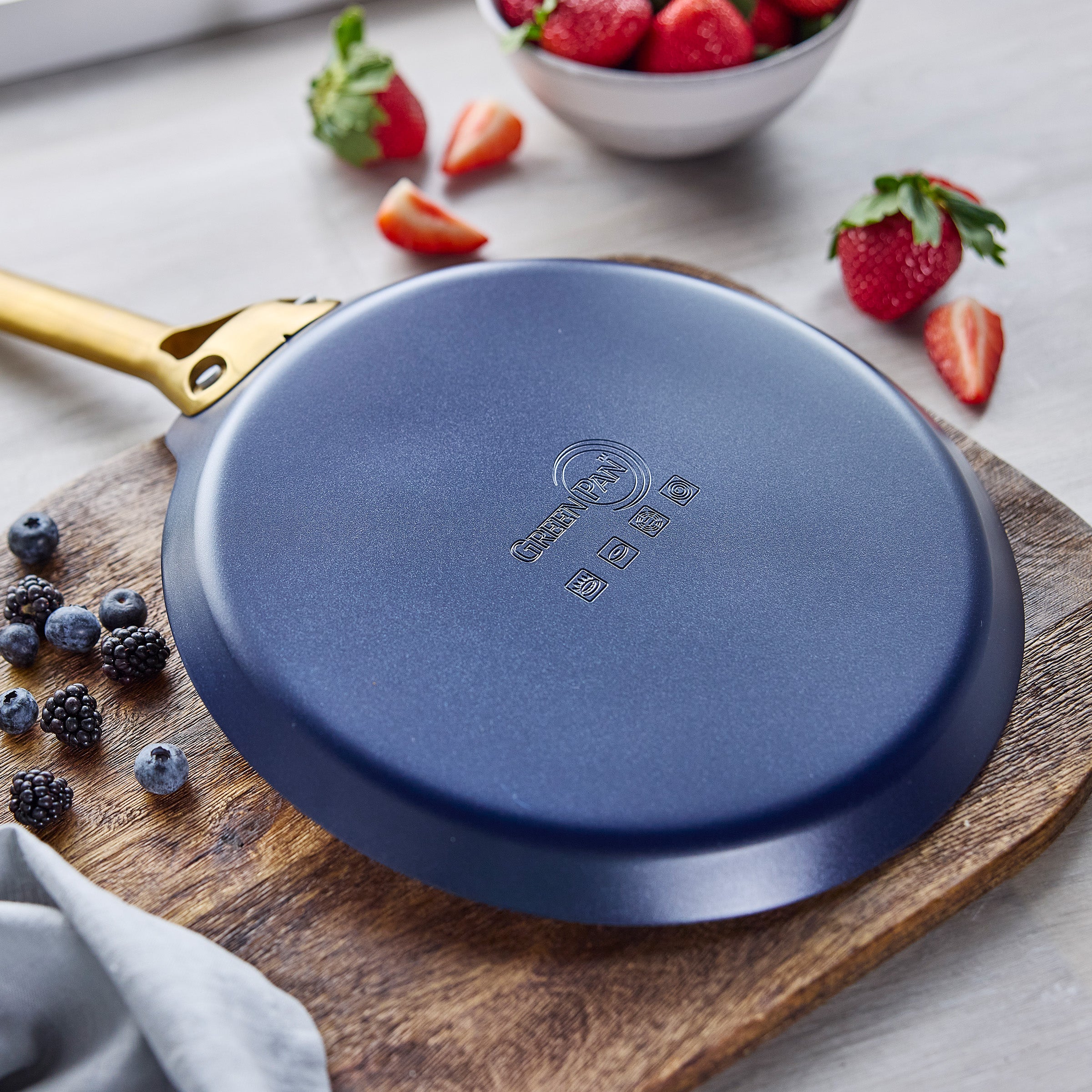 Blue crepe pan on a wooden board with berries in the background