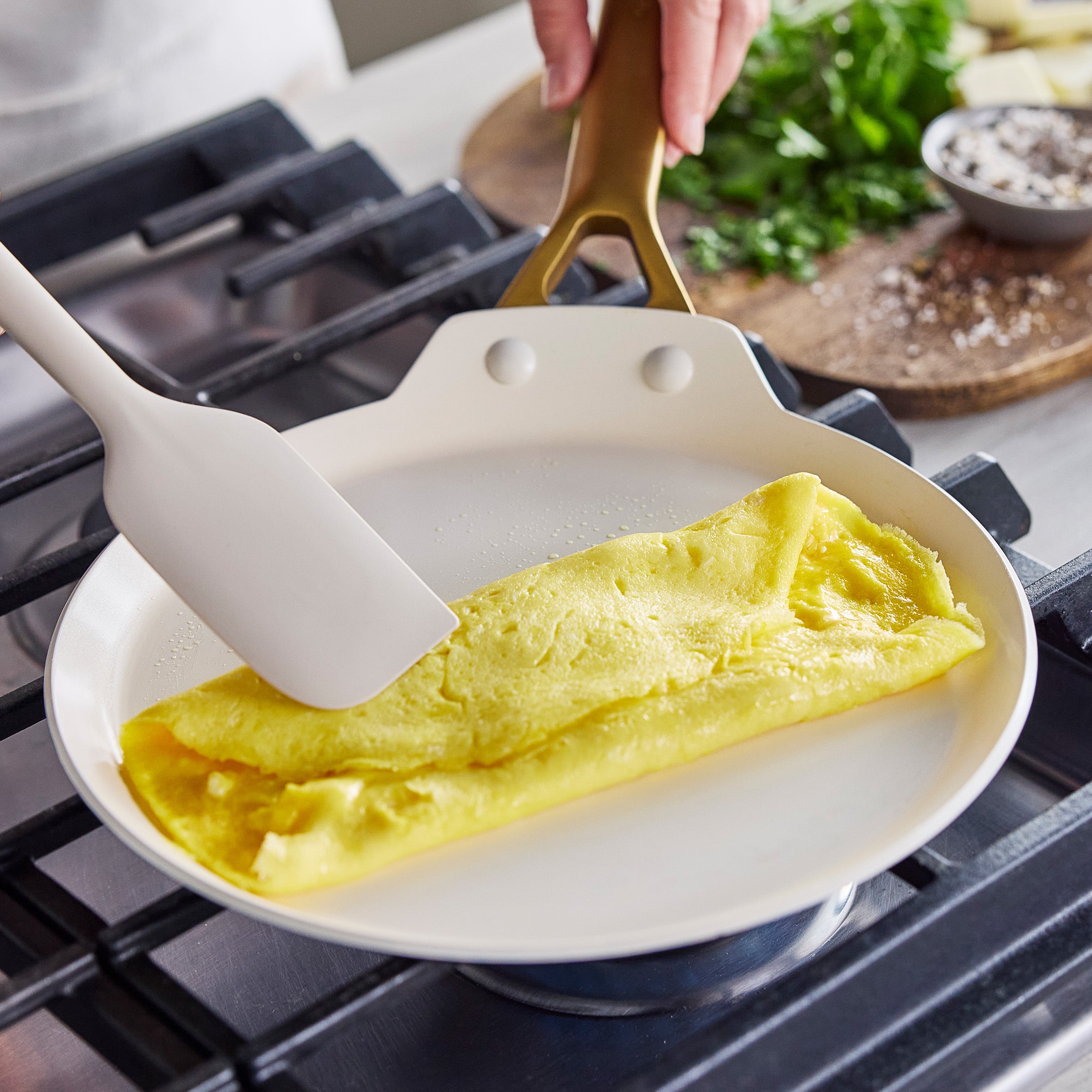 Omelette being folded in a crepe pan with a spatula on a stove.