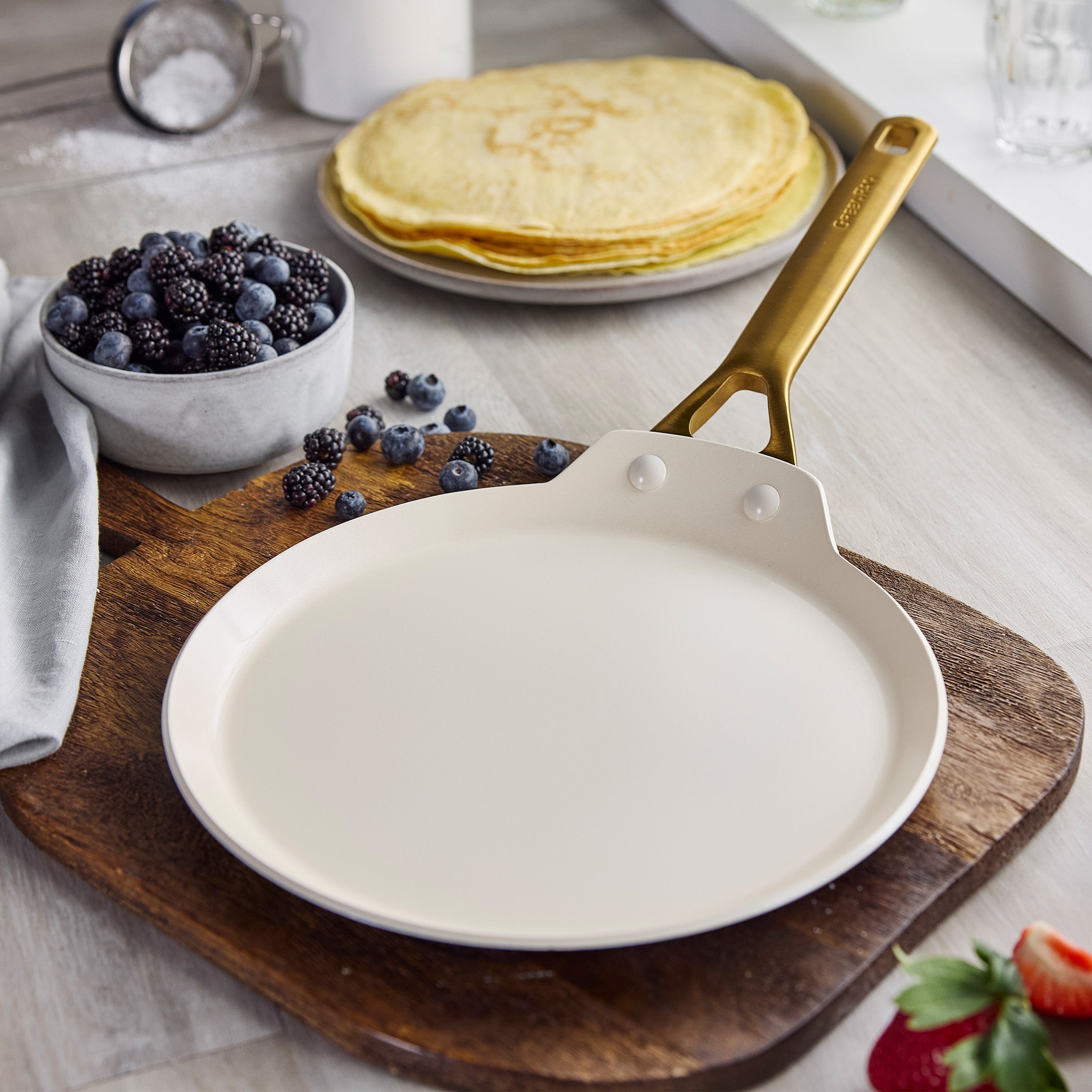Crepe pan on wooden board with crepes and berries the background