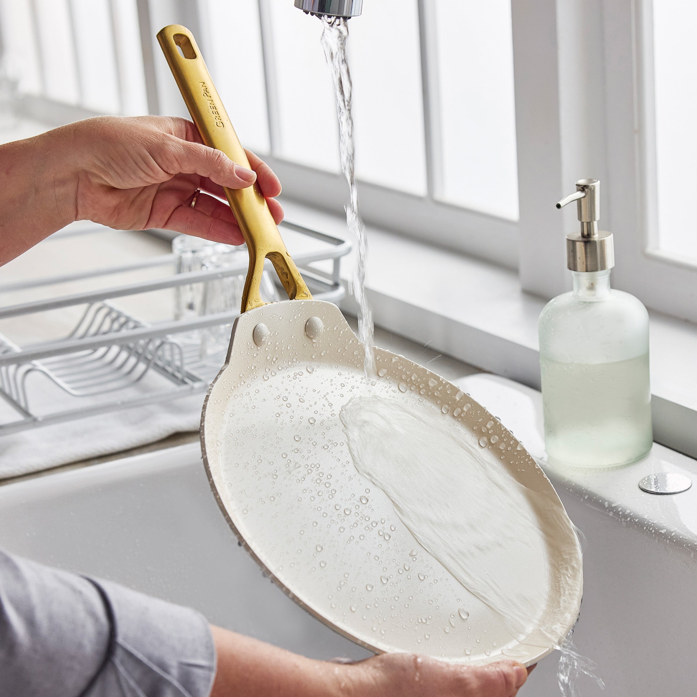 Person washing a crepe pan under running water in a kitchen sink