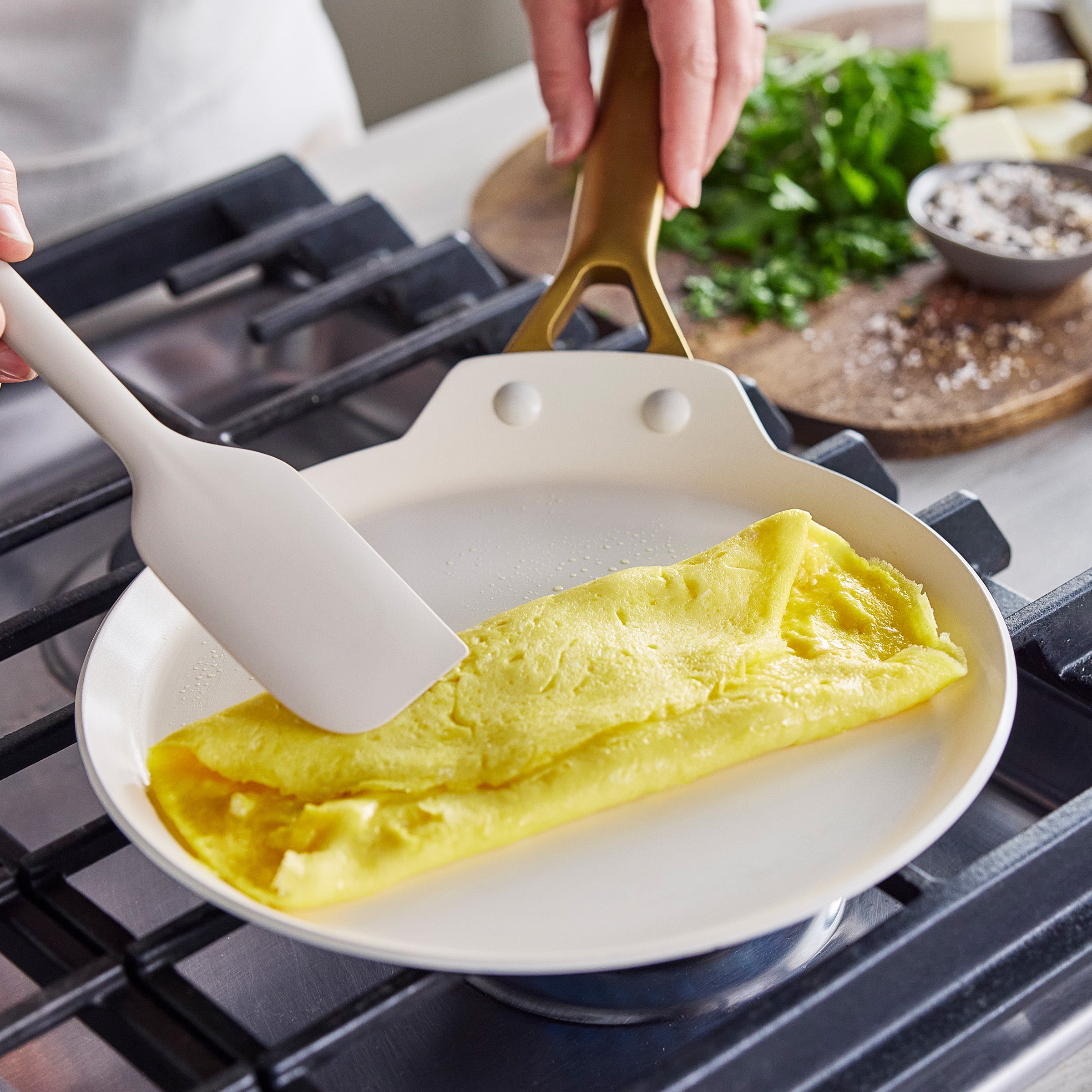 Omelette being folded in a crepe pan with a spatula on a stove.