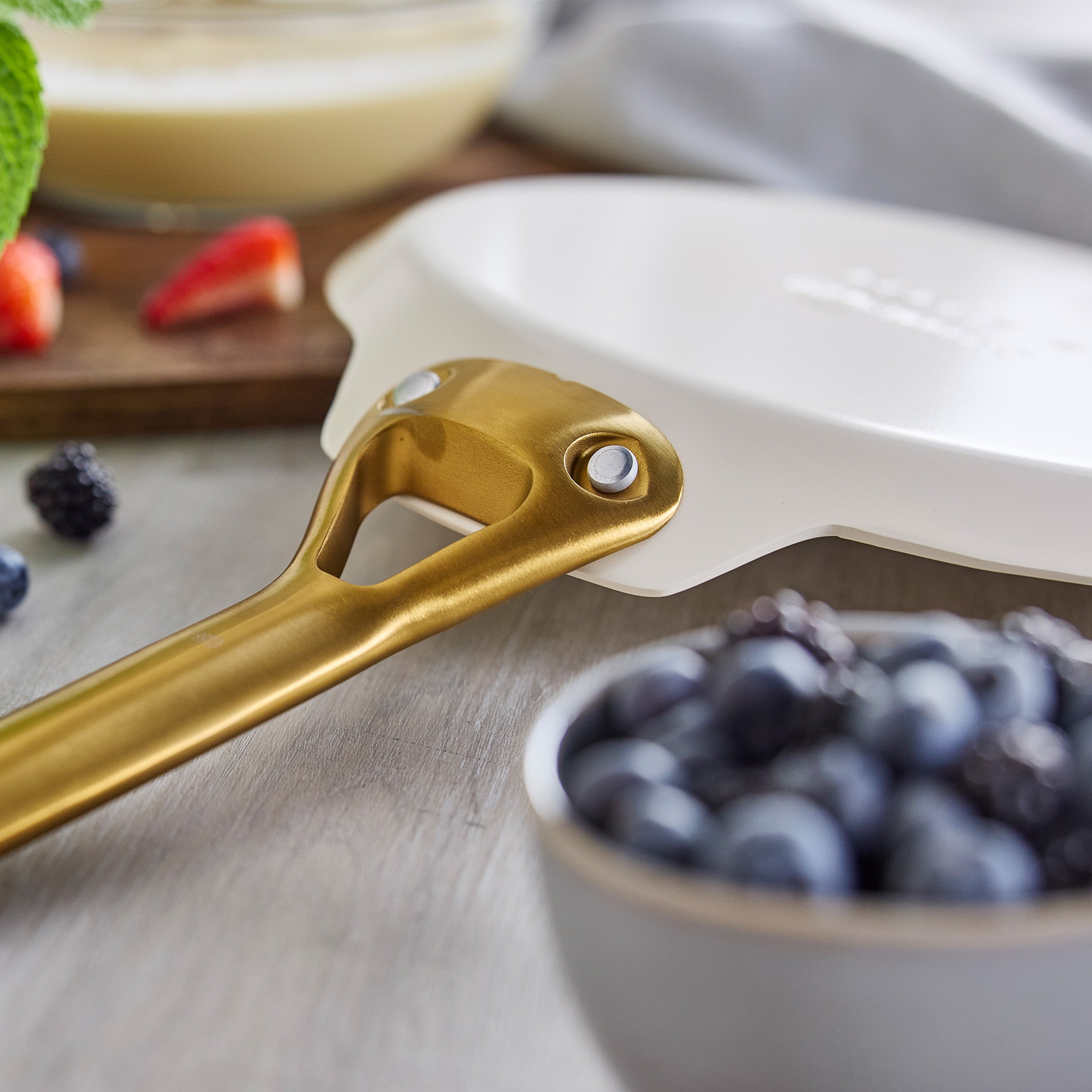 Gold-handled crepe pan with berries in the background