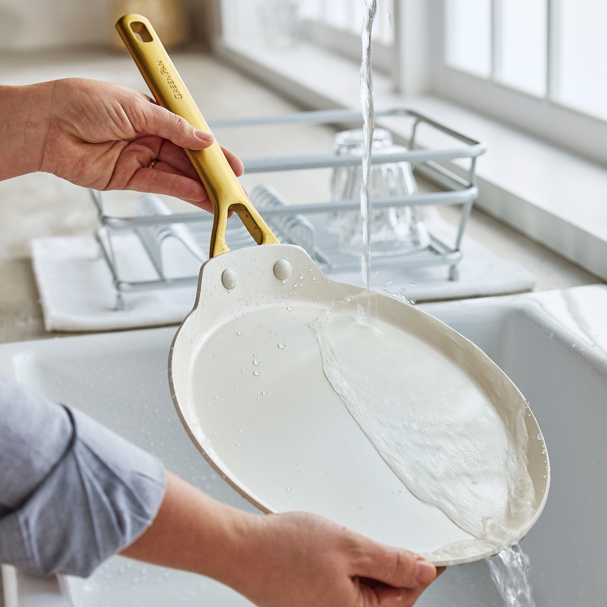 Person washing a crepe pan under running water in a kitchen sink