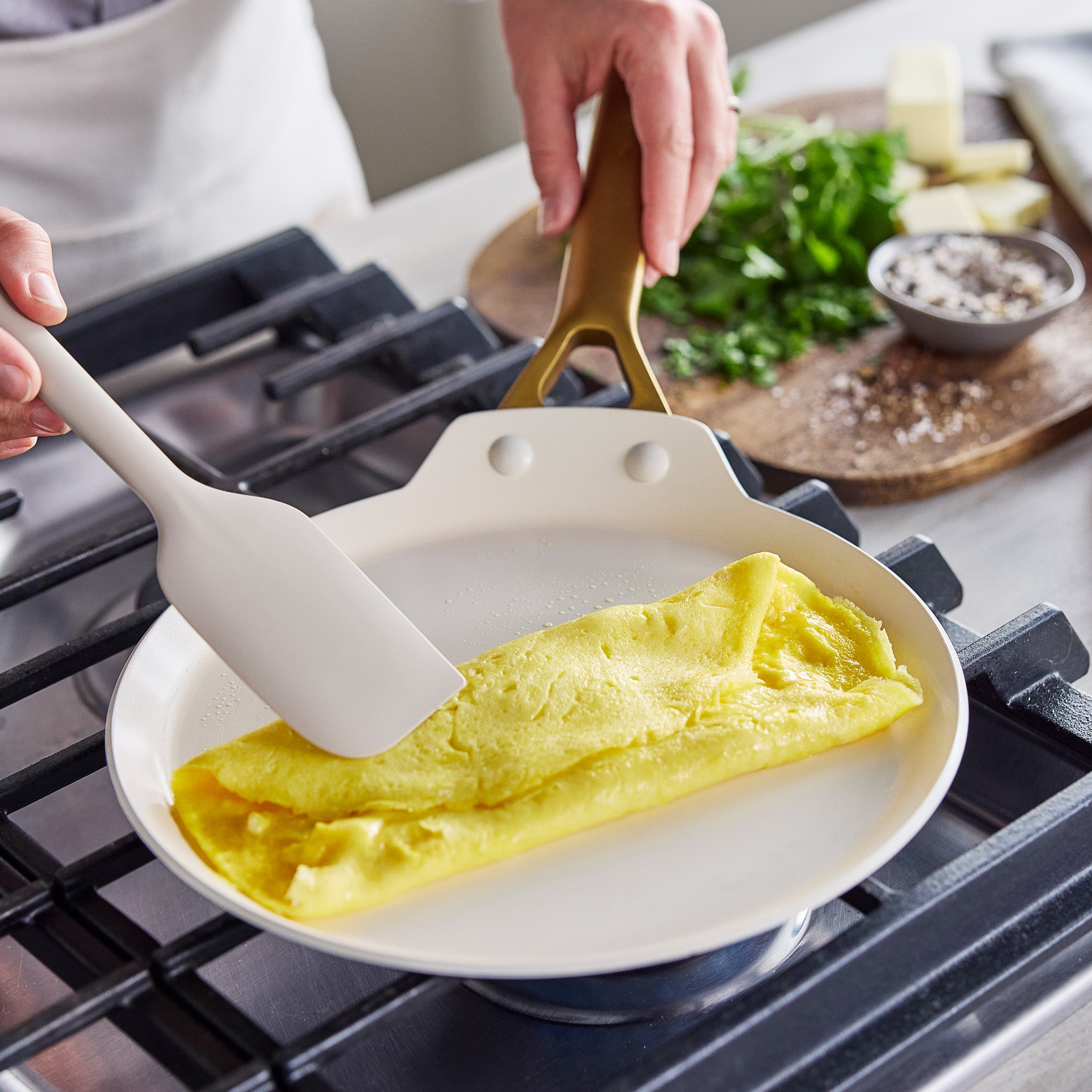 Person folding an omelette in a crepe pan on a stove with a spatula.