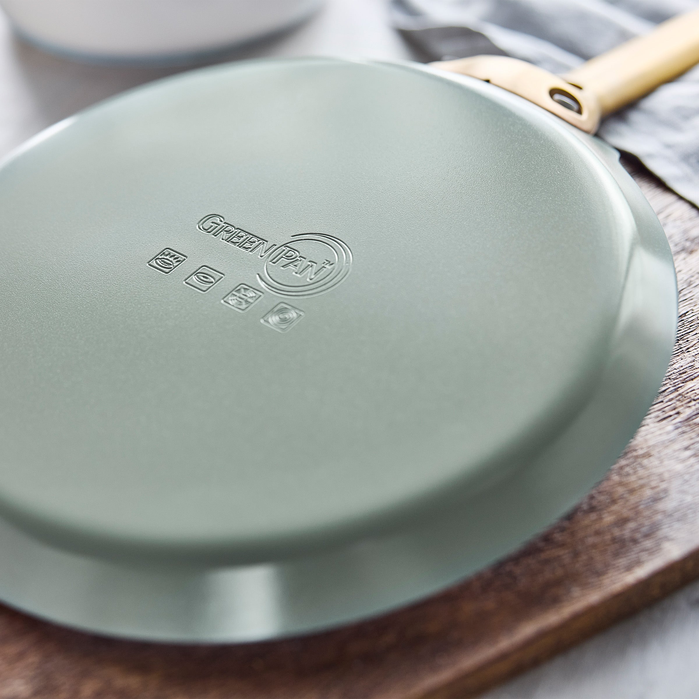 Green crepe pan with a gold handle on a wooden surface