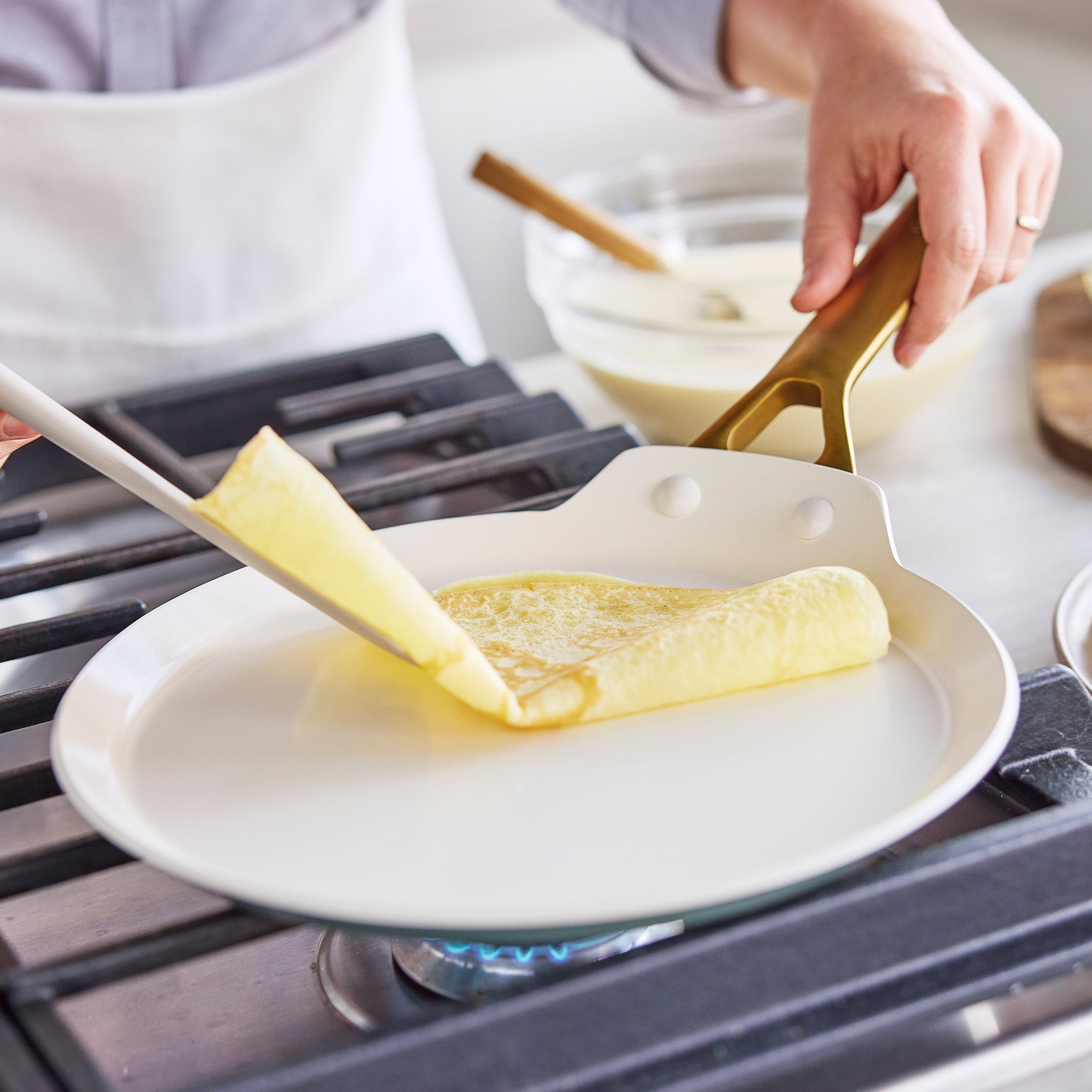 Person cooking a crepe on a stove using a spatula.
