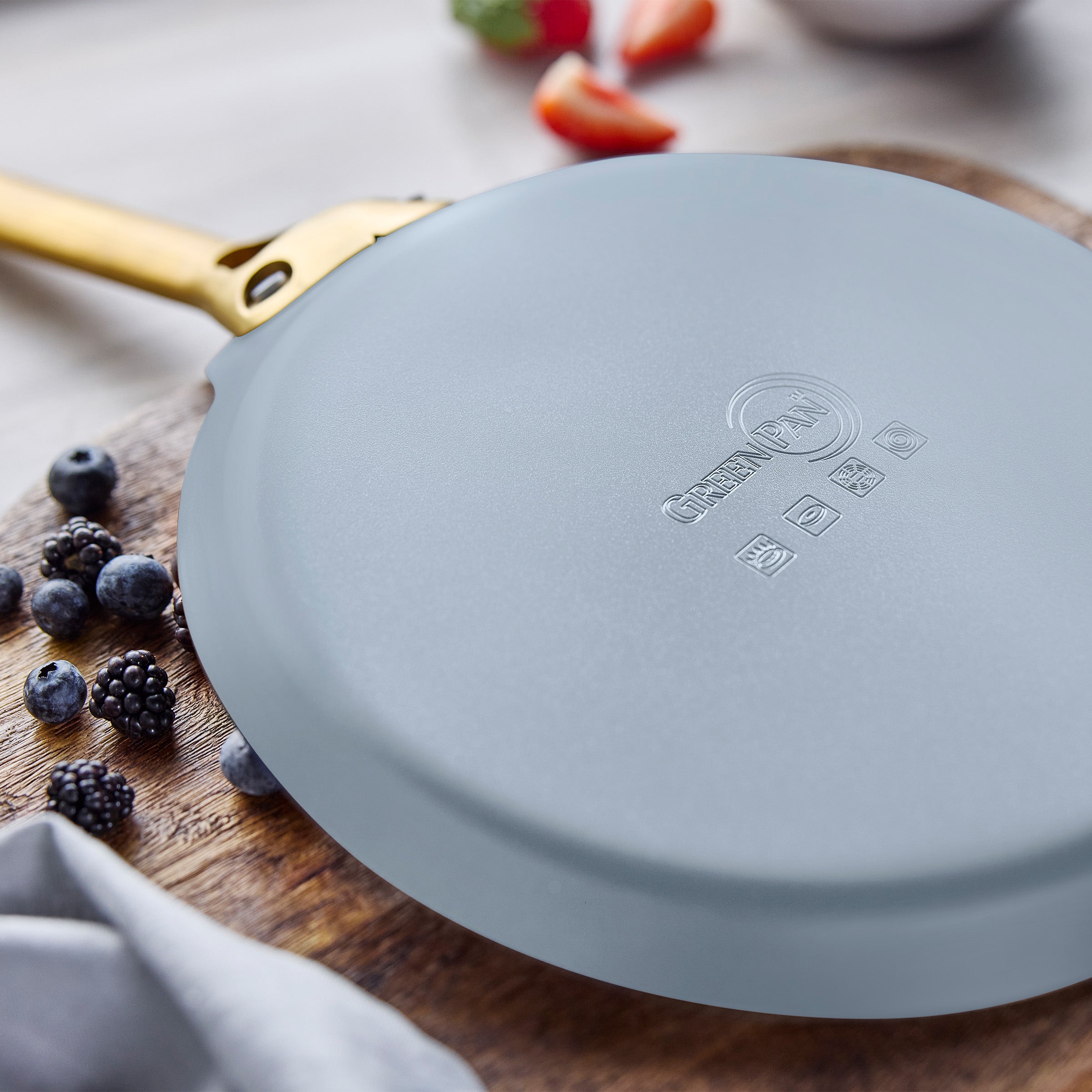 Blue crepe pan on a wooden surface with berries and a blurred background