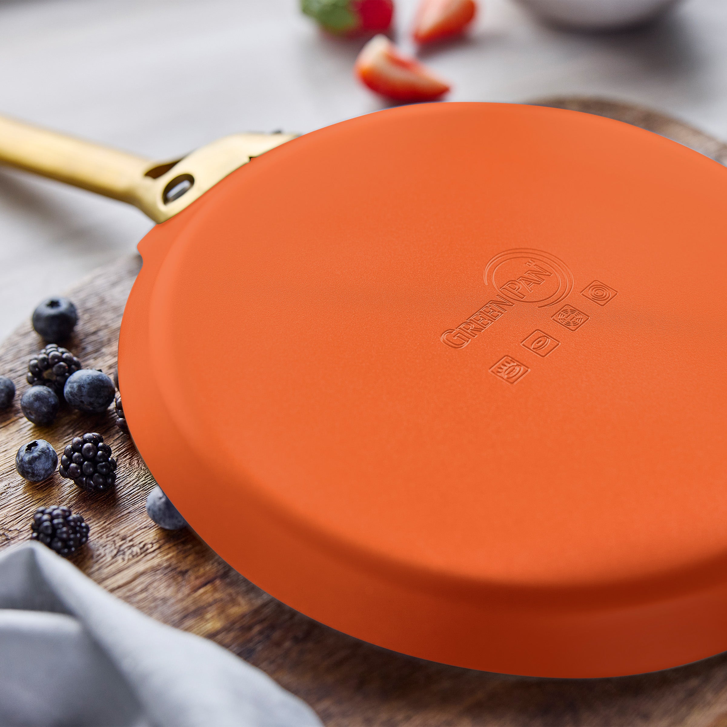 Orange crepe pan on a wooden surface with berries and a cloth.