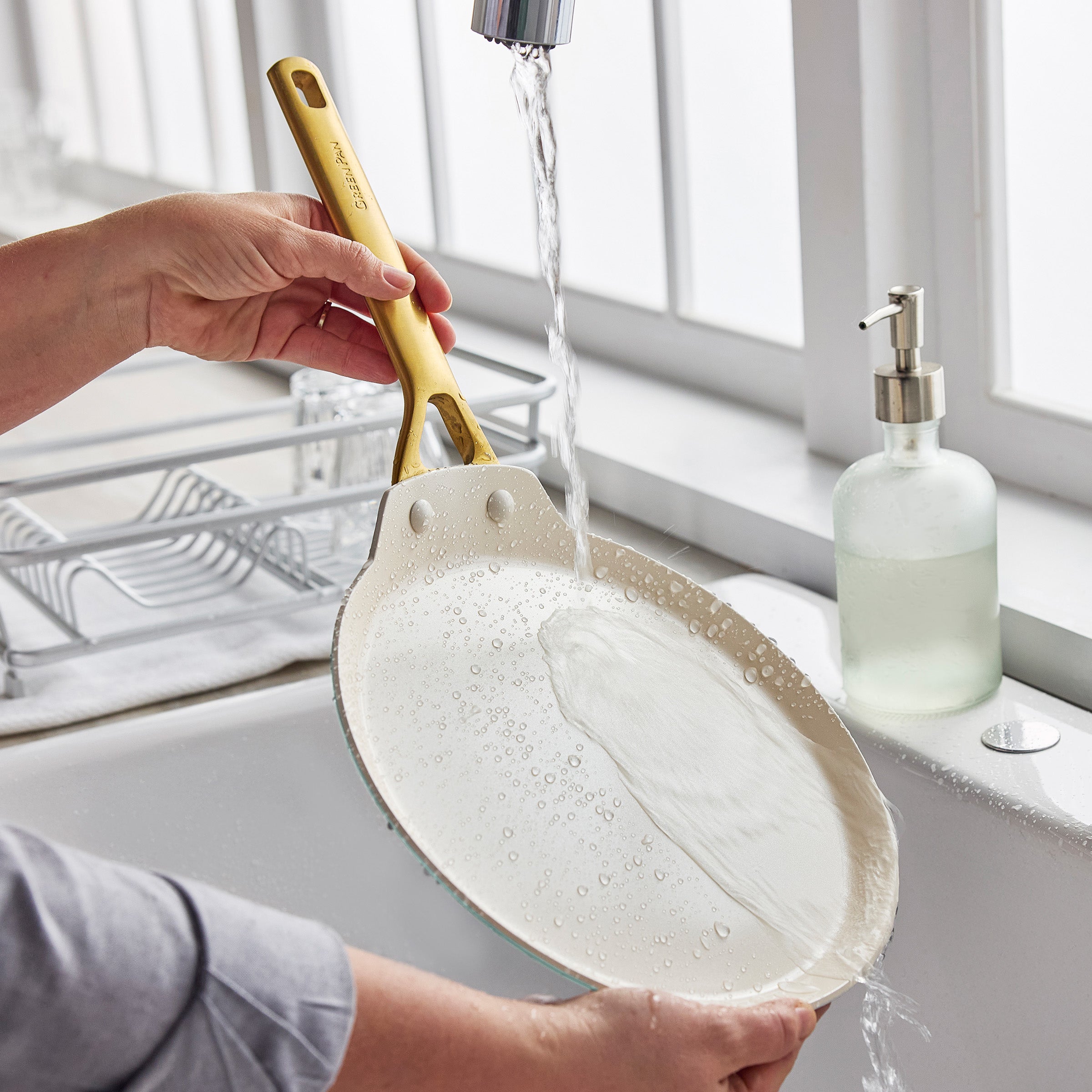 Person washing a crepe pan under running water with soap in a kitchen sink